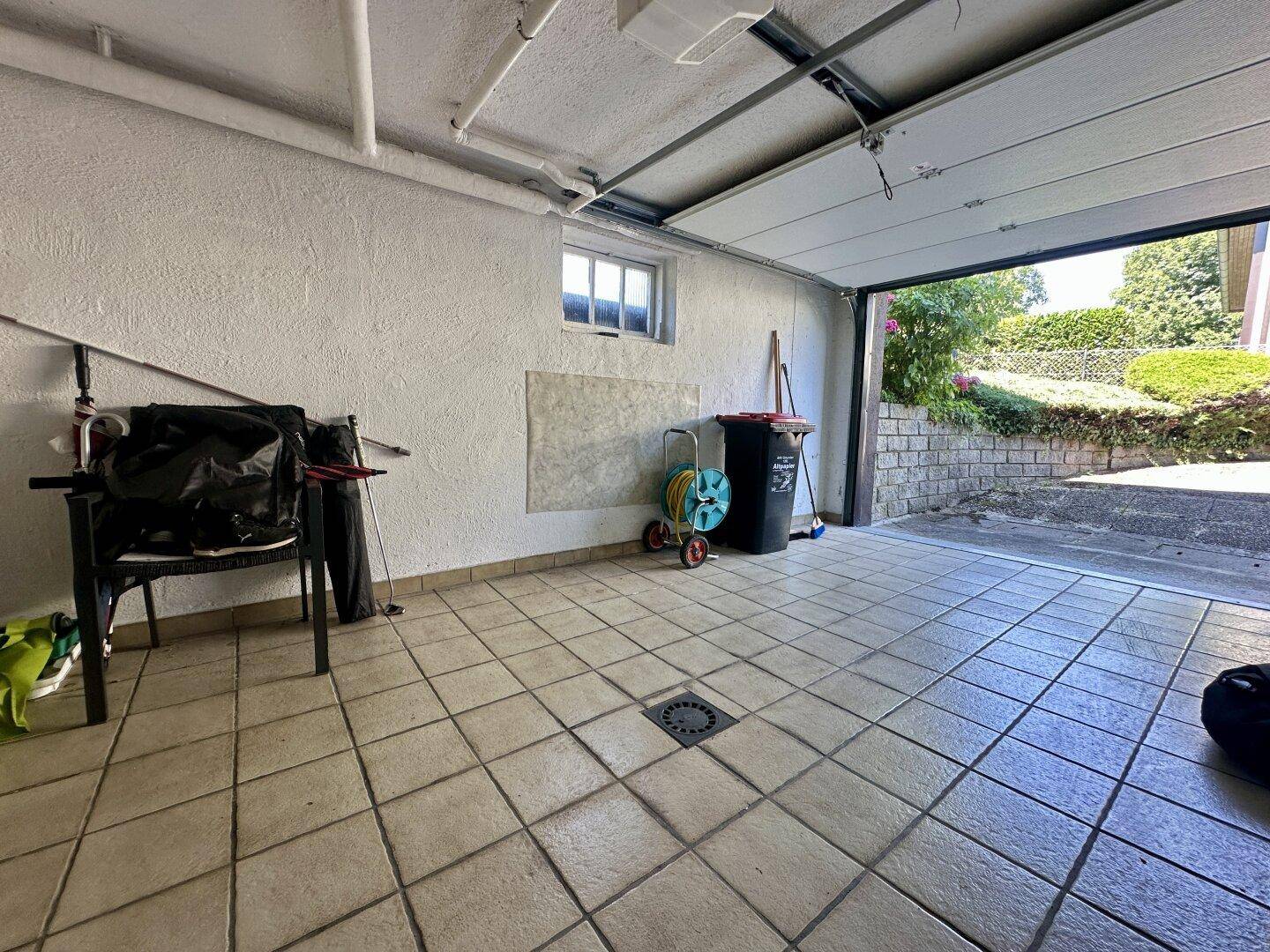 Garage mit Fliesenboden, Werkzeugen und Blick nach draußen.
