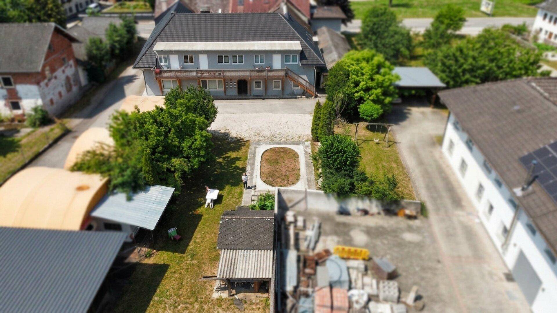 Luftaufnahme des Hauptgebäudes mit großem gepflasterten Vorplatz und einer ovalen Rasenfläche im Zentrum.