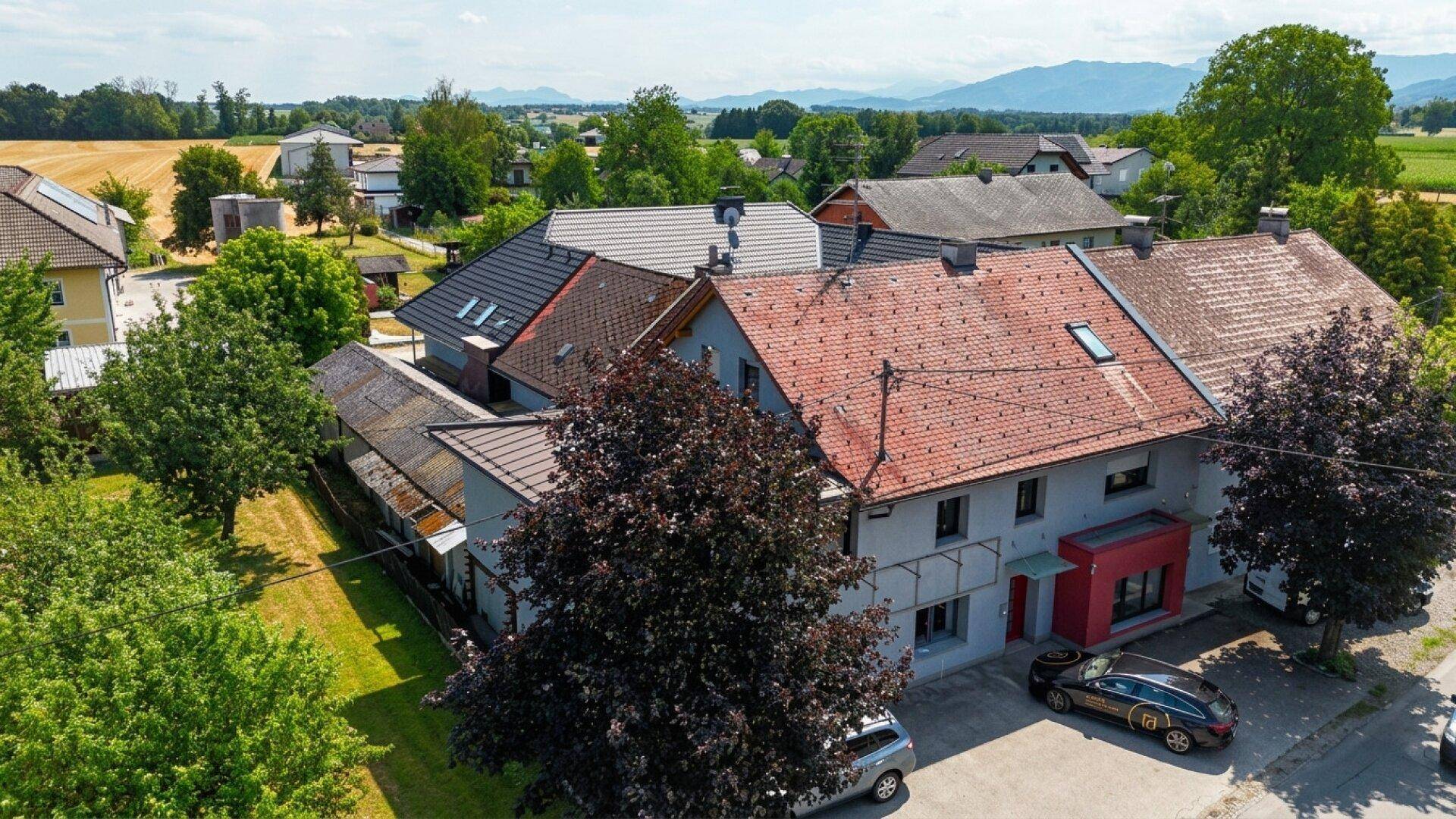 Weitläufige Luftaufnahme des älteren Gebäudeteils mit rotem Dach und ländlicher Umgebung mit Feldern und Bergen.