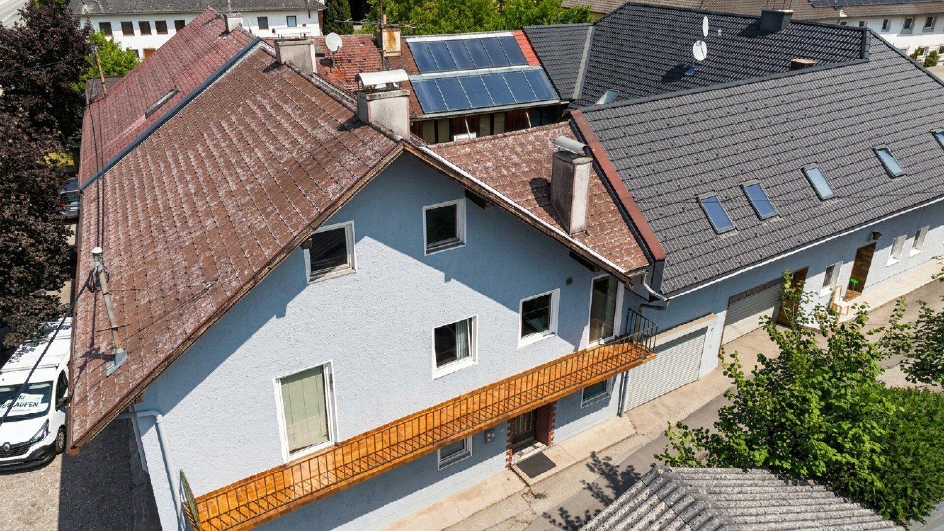 Luftaufnahme eines Gebäudes mit heller Fassade, rotem Ziegeldach und einem langen, schmalen Balkon mit Metallgeländer.
