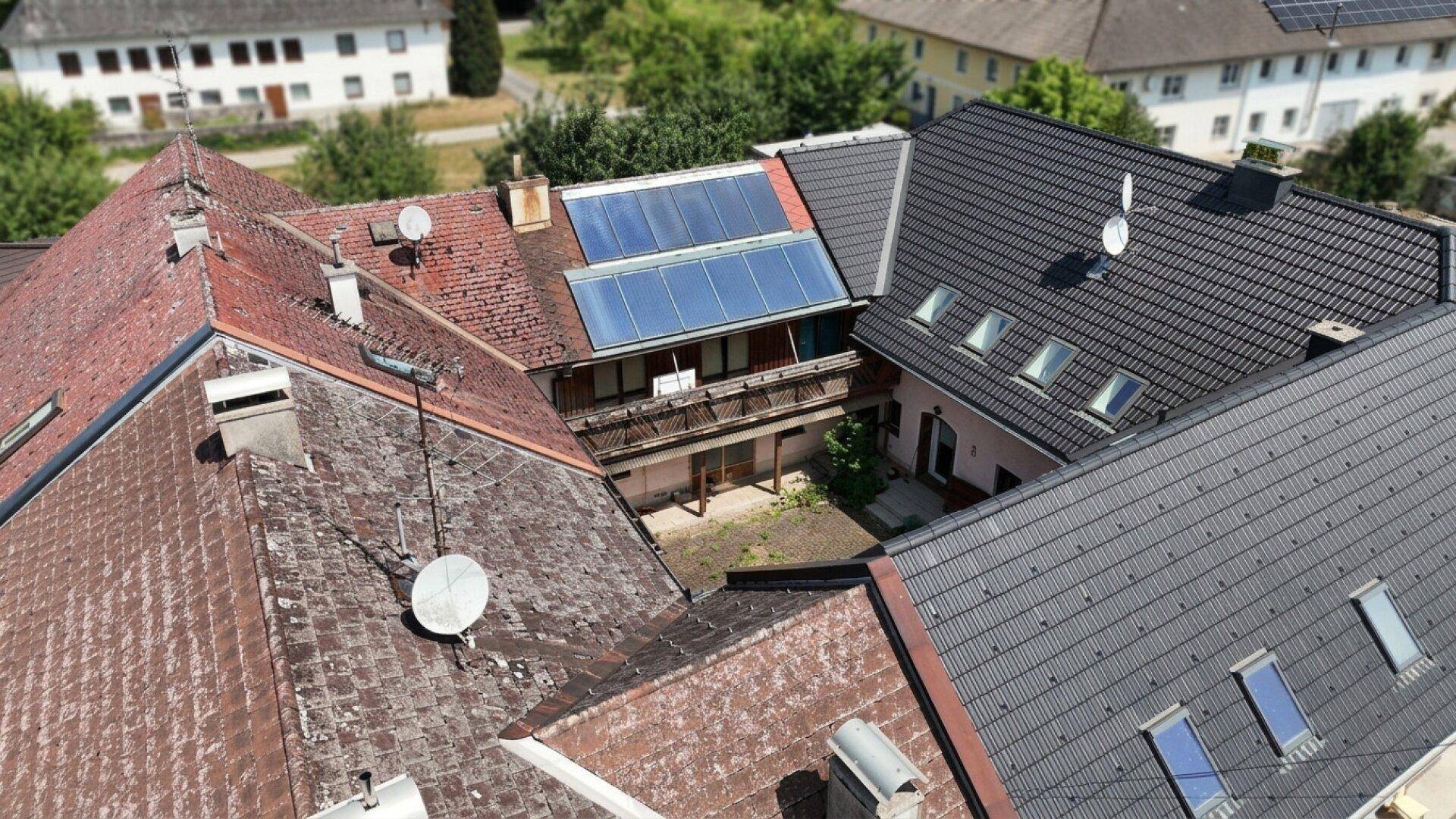 Dachlandschaft verschiedener Gebäude mit dunklen und roten Ziegeldächern, teilweise mit Solarpaneelen und Dachfenstern.