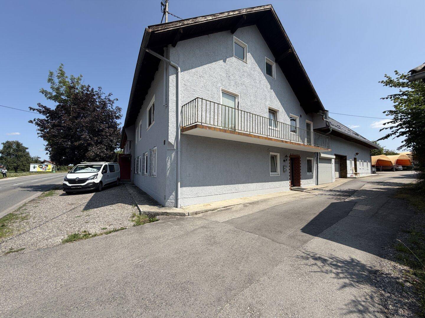 Seitenansicht des Gebäudes mit heller Fassade, rotem Ziegeldach und einem langen Balkon mit schwarzem Metallgeländer.