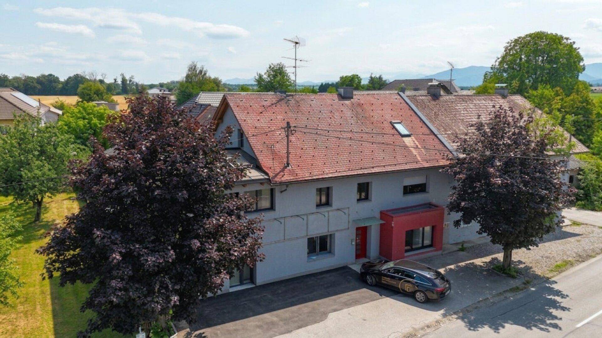 Luftaufnahme eines älteren Gebäudeteils mit rotem Ziegeldach, grauer Fassade und rotem Eingangsbereich.