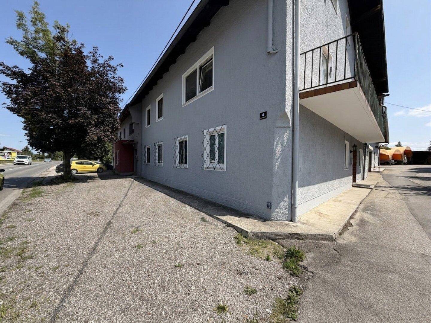 Nahaufnahme der Gebäudeseite mit heller Fassade und dem schmalen Balkon mit Metallgeländer, angrenzend an eine Straße.