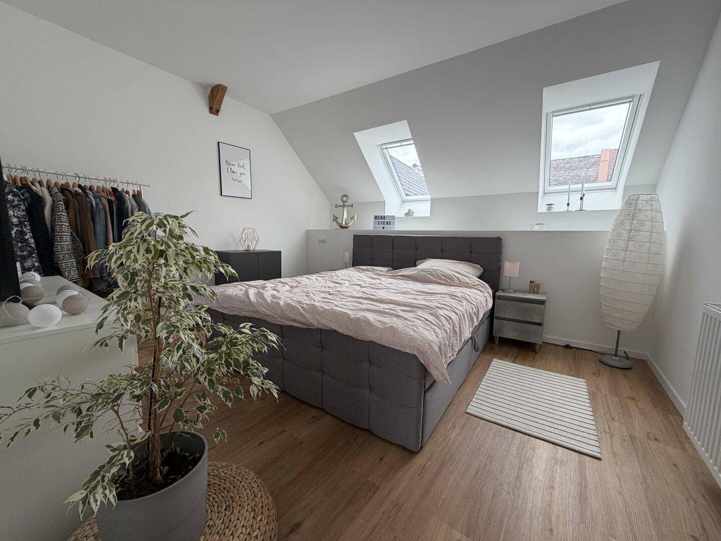 Helles Schlafzimmer im Dachgeschoss mit schrägen Wänden, zwei Dachfenstern und modernem Doppelbett.