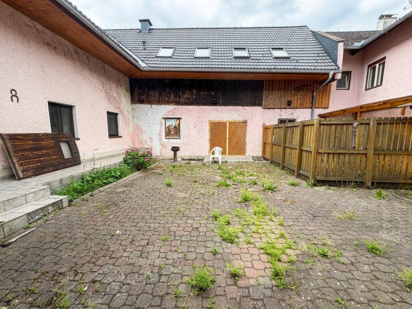 Innenhof mit Kopfsteinpflaster, rosa Fassade und Holzelementen, umgeben von einem Holzzaun.