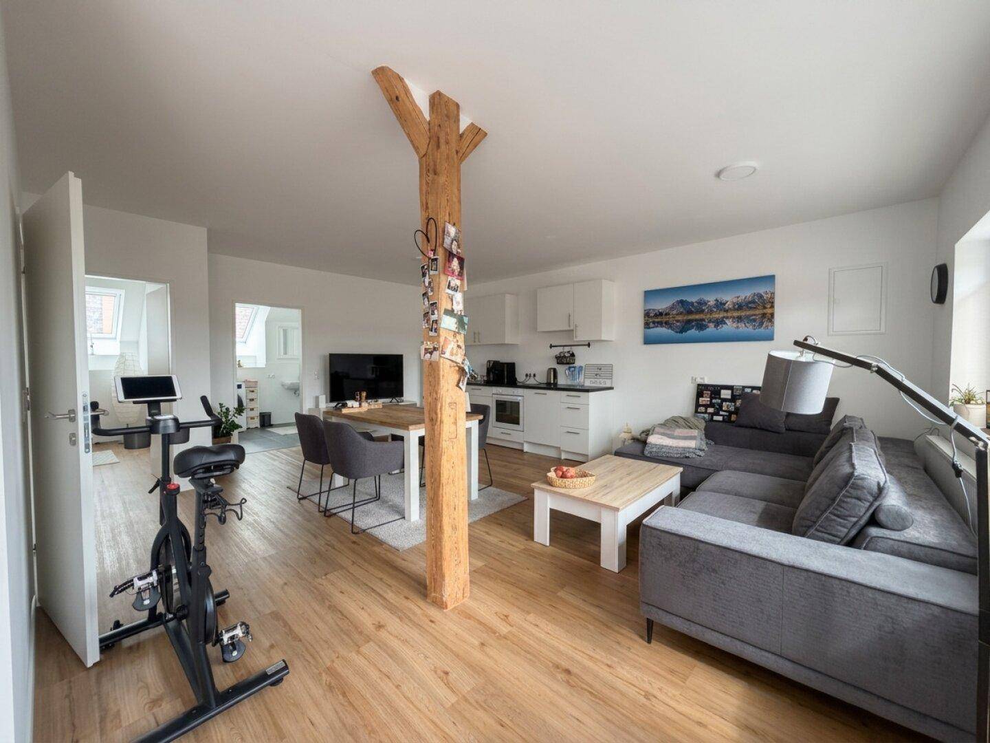 Heller Wohn-Essbereich mit integrierter Küche, Holzboden und modernem Mobiliar, inklusive Fitnessgerät.