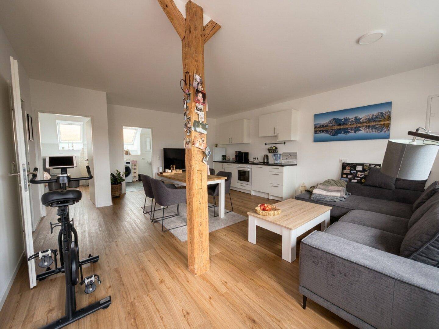Offener Wohn-Essbereich mit Holzboden, moderner Küche, gemütlichem Sofa und einem dekorativen Holzpfosten.