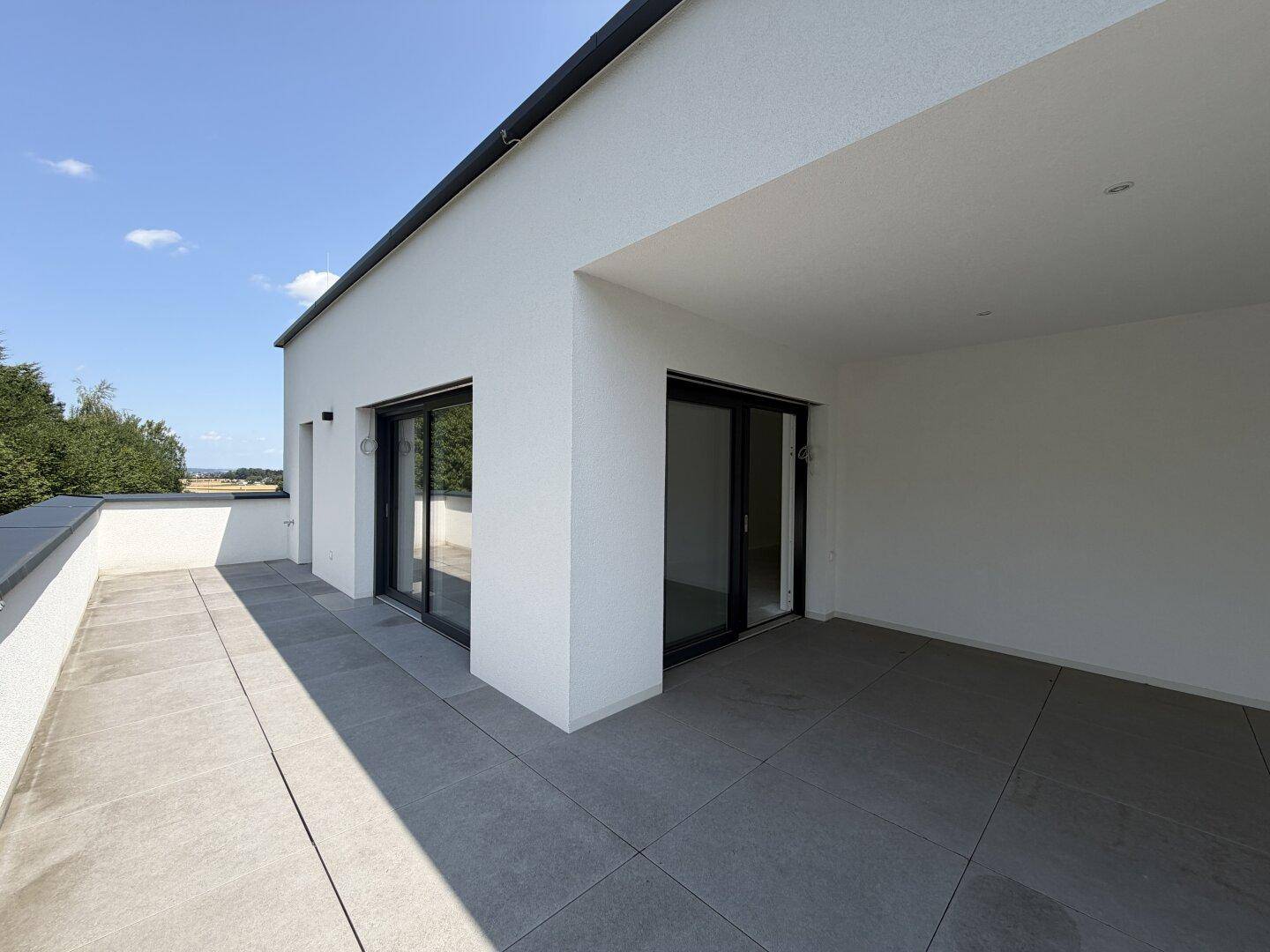 Weitläufige, geflieste Terrasse mit Zugang zu mehreren Räumen und Blick auf die Umgebung.