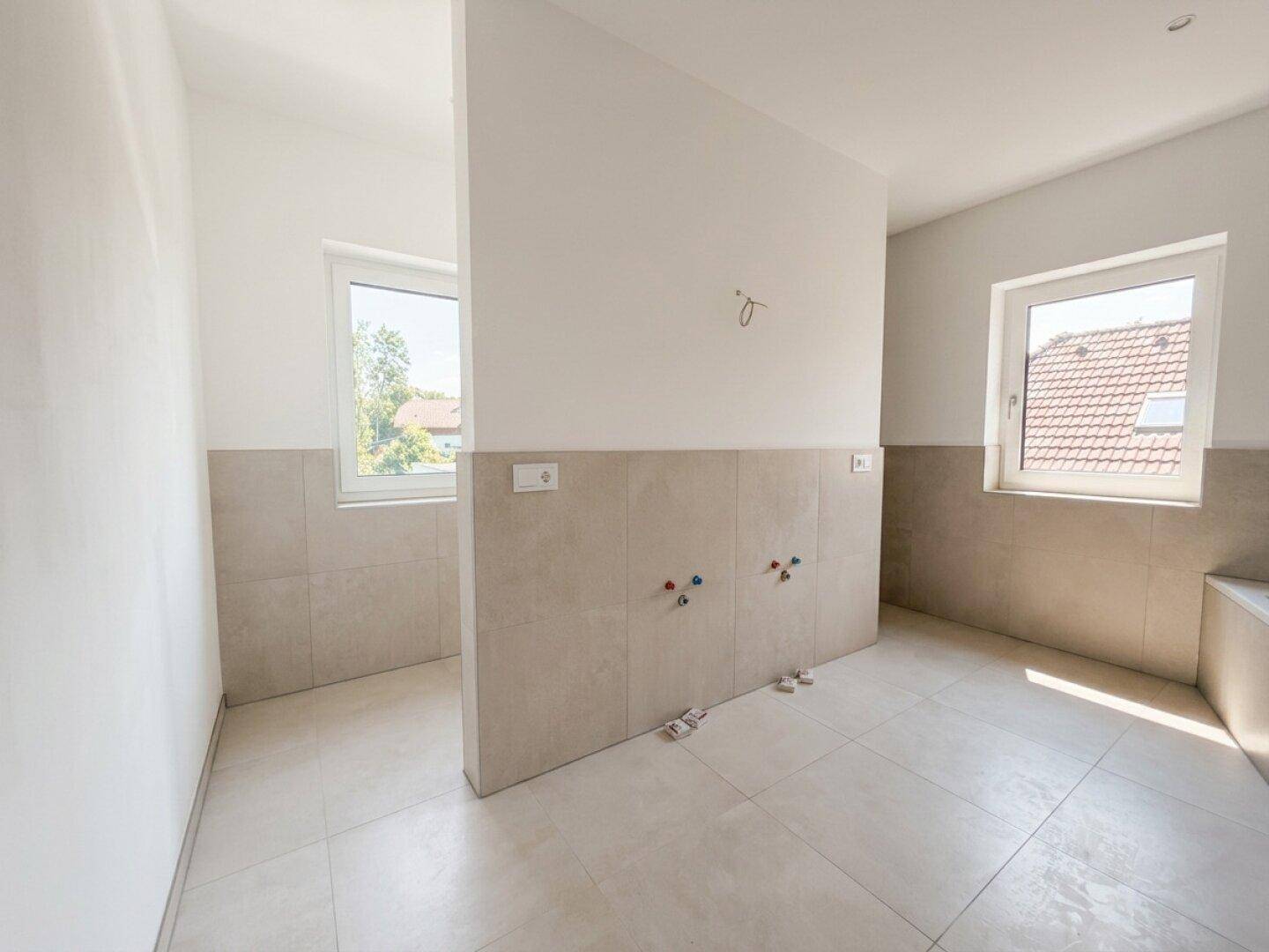 Geräumiges Badezimmer im Rohbau mit vorbereiteten Anschlüssen für Doppelwaschbecken und Badewanne.