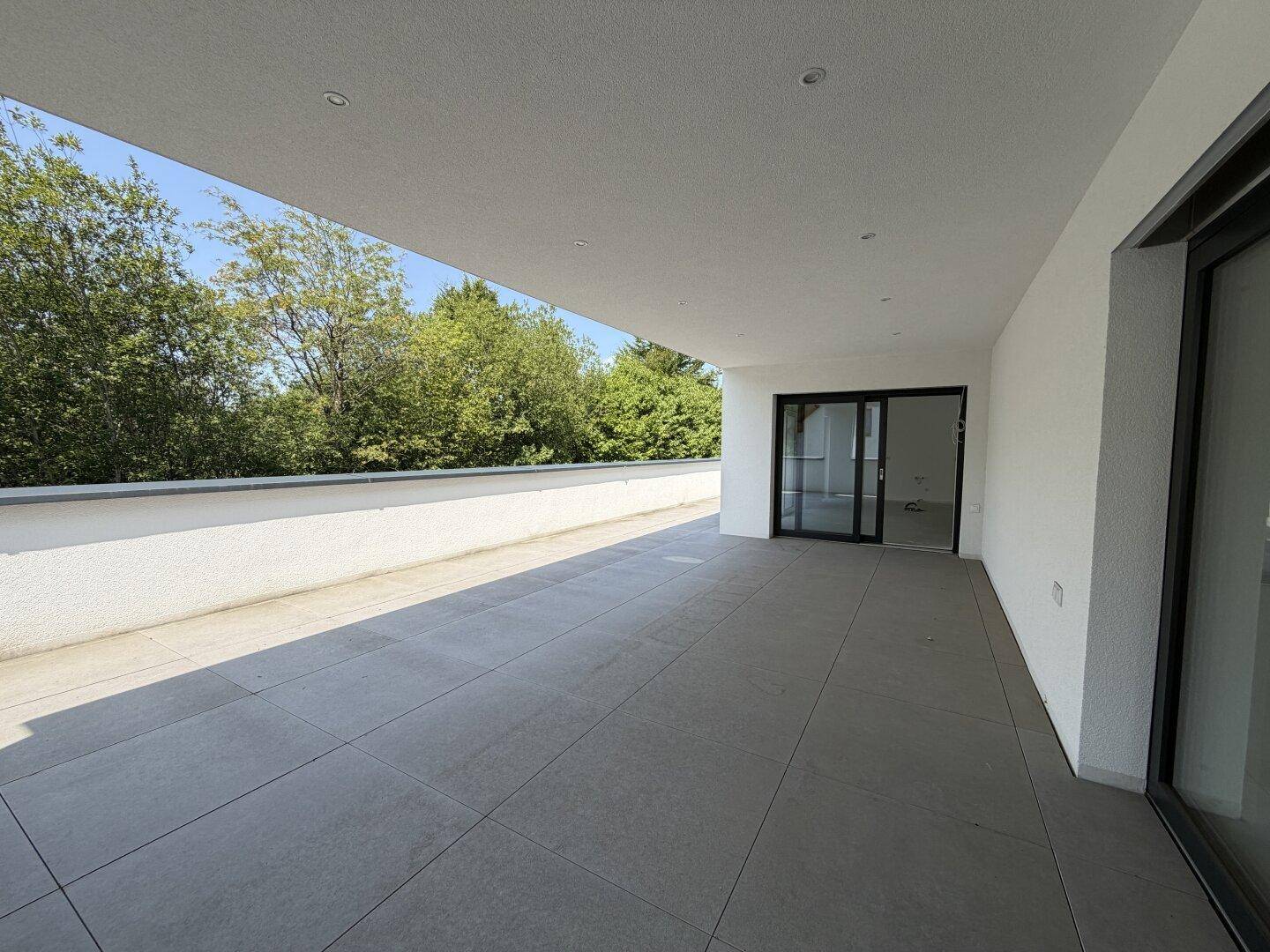 Breite, geflieste Terrasse mit viel Tageslicht und direktem Zugang zu den Innenräumen.