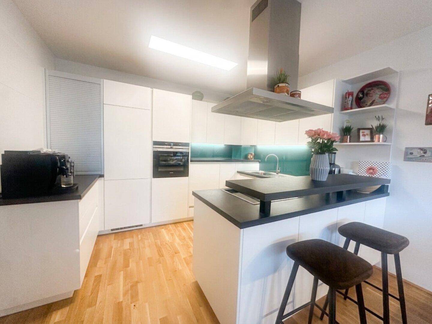 Moderne weiße Küche mit Kochinsel, dunkler Arbeitsplatte und Holzboden.