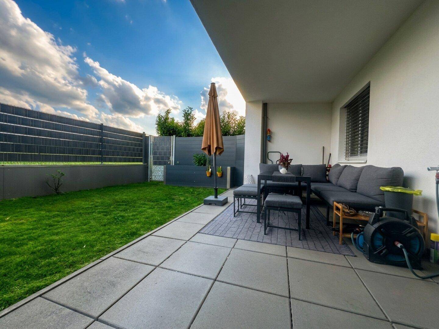 Sonniger Terrassenbereich mit Gartenmöbeln und Blick auf den privaten Garten.
