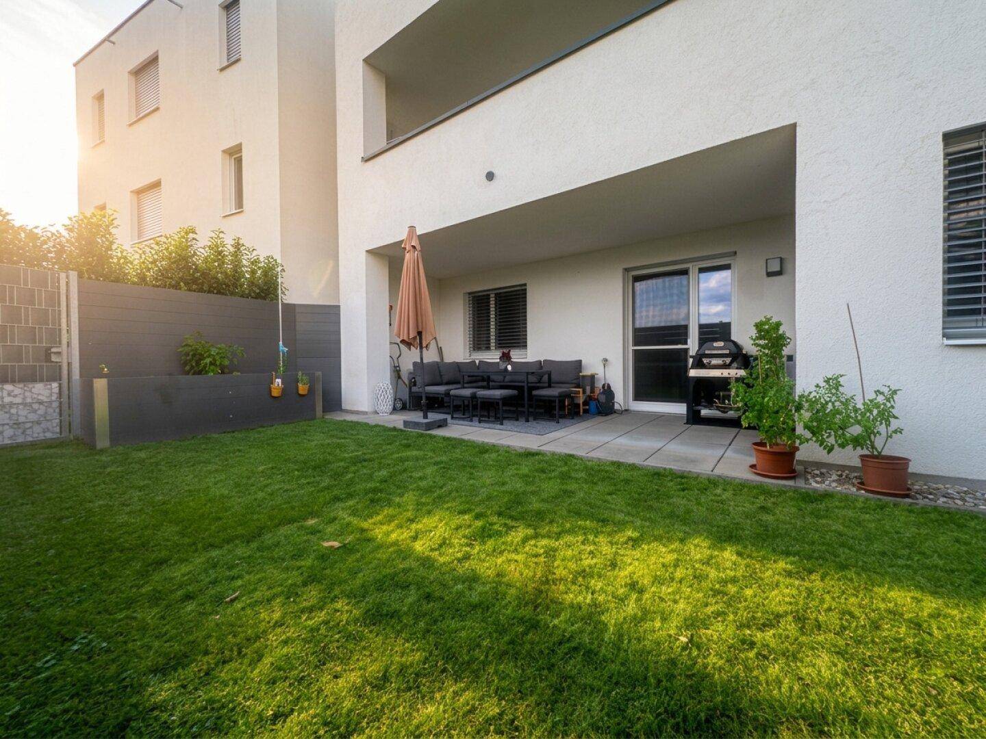 Gepflegter Gartenbereich mit Rasenfläche und angrenzender Terrasse mit Sitzgelegenheiten.
