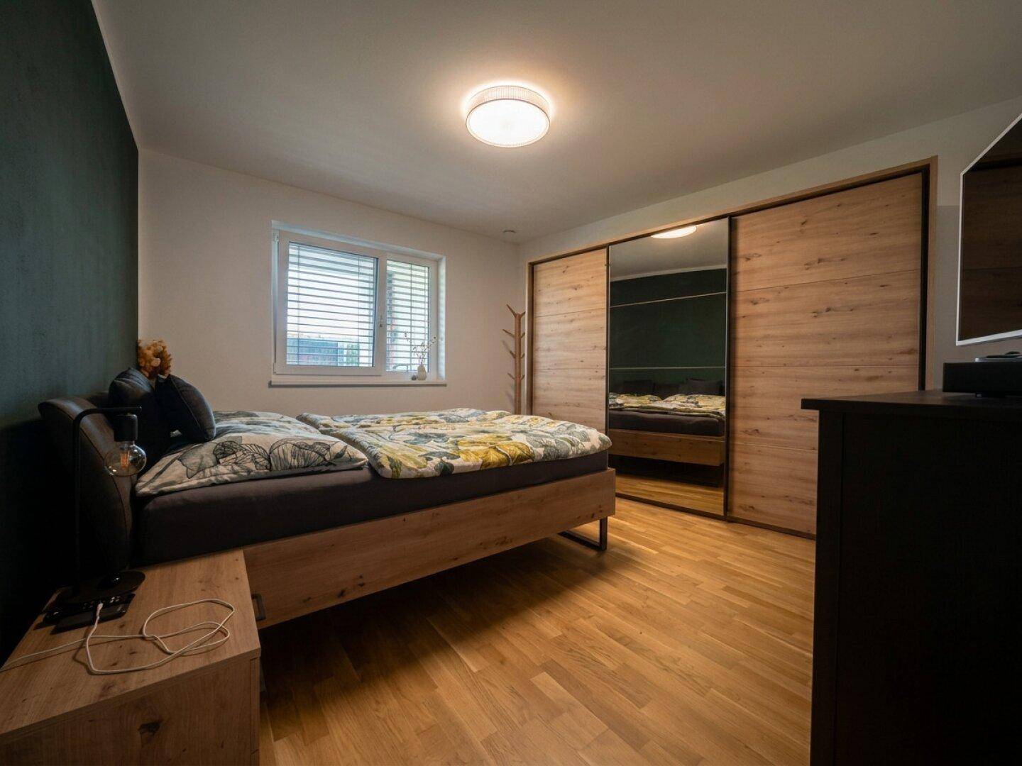 Schlafzimmer mit Holzbett, großem Spiegelschrank und Parkettboden.