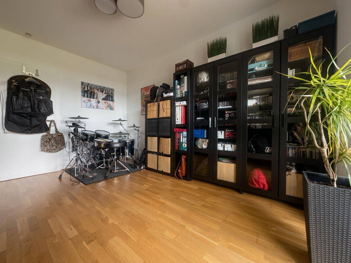 Geräumiges Zimmer mit Holzboden, schwarzen Regalen und Schlagzeug.