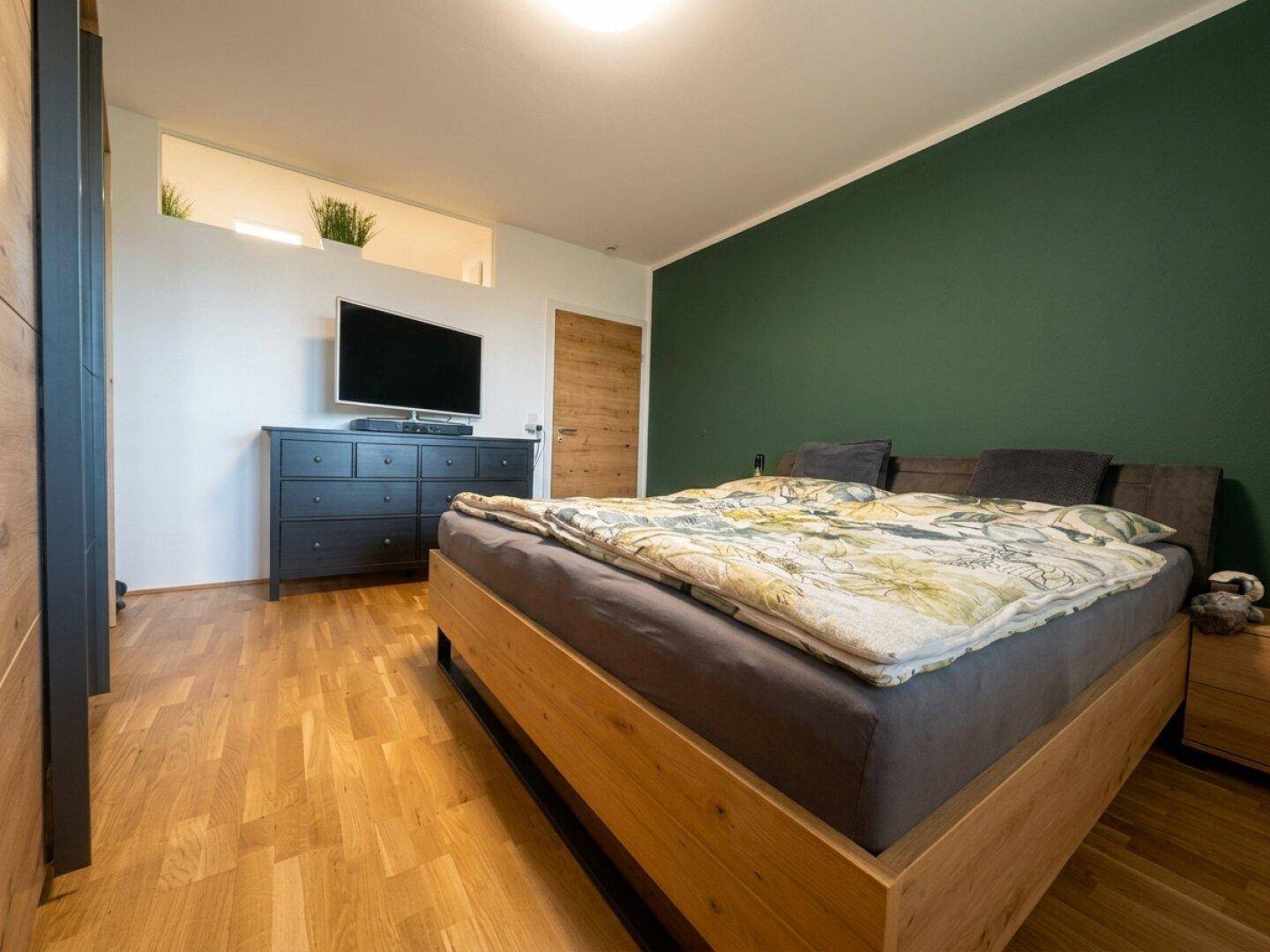Schlafzimmer mit Holzbett, grüner Akzentwand und Parkettboden.