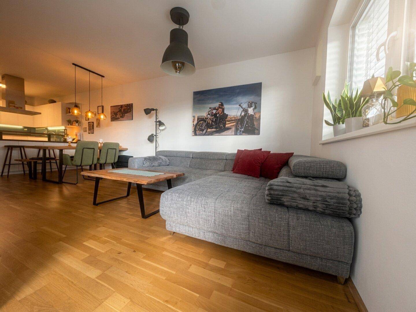 Gemütliches Wohnzimmer mit Ecksofa, Holzboden und viel Tageslicht.