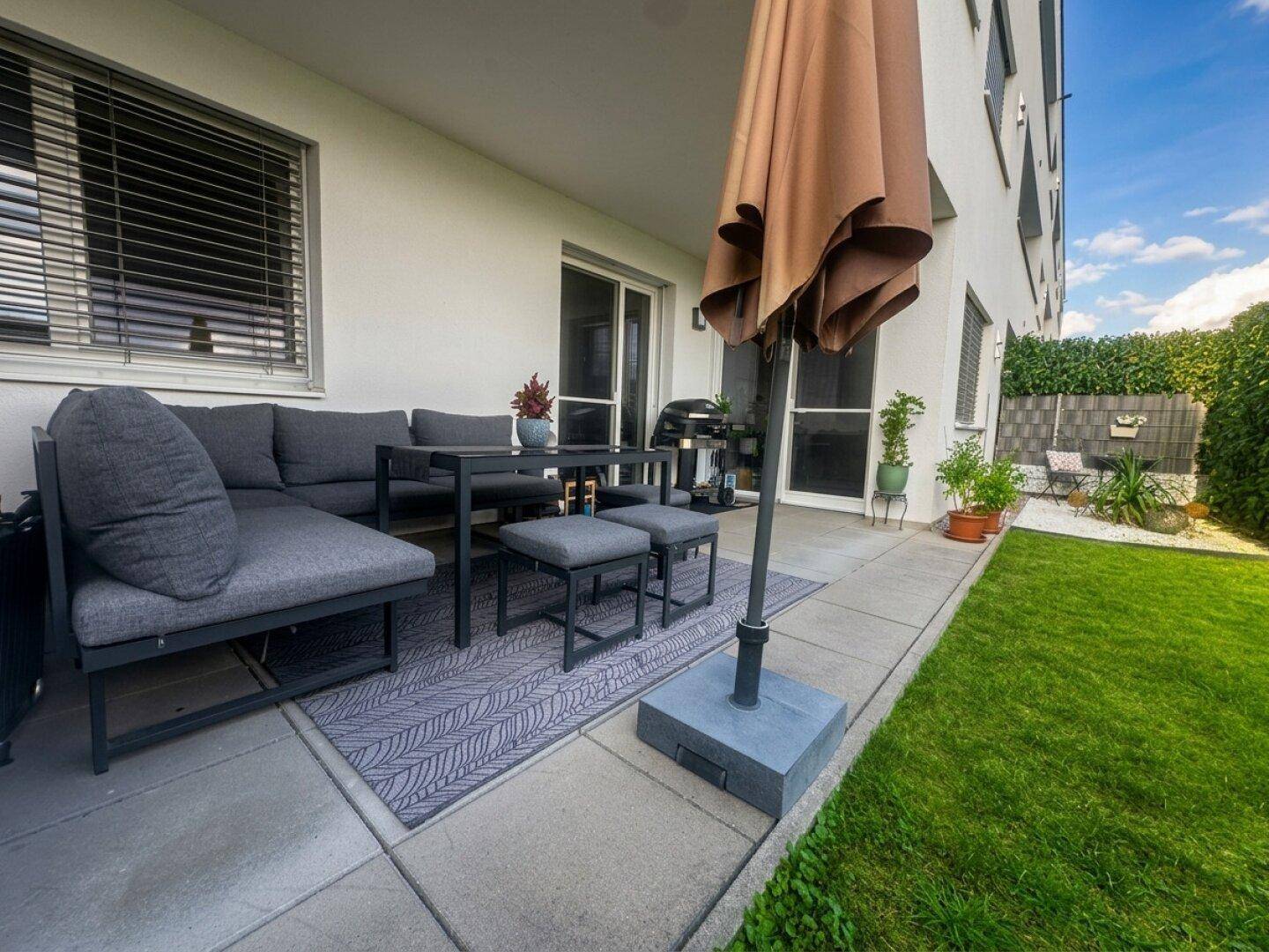 Geräumige Terrasse mit Sitzgruppe und Sonnenschirm, angrenzend an den Garten.