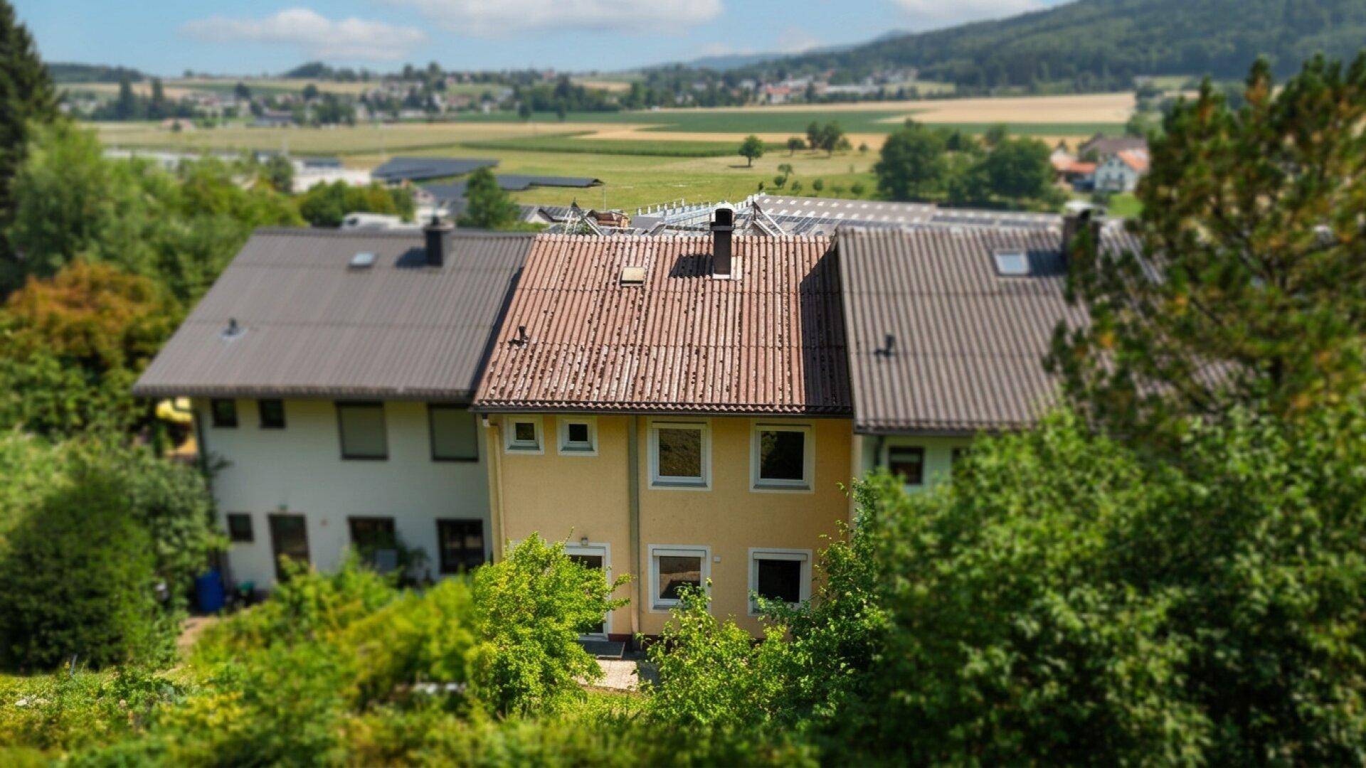 Reihenhäuser eingebettet in eine grüne Landschaft mit Feldern und Wäldern im Hintergrund.