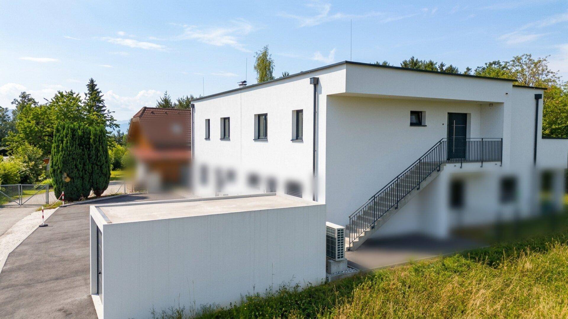 Ansicht des modernen Neubaus mit schlichter weißer Fassade und umliegender Grünfläche.