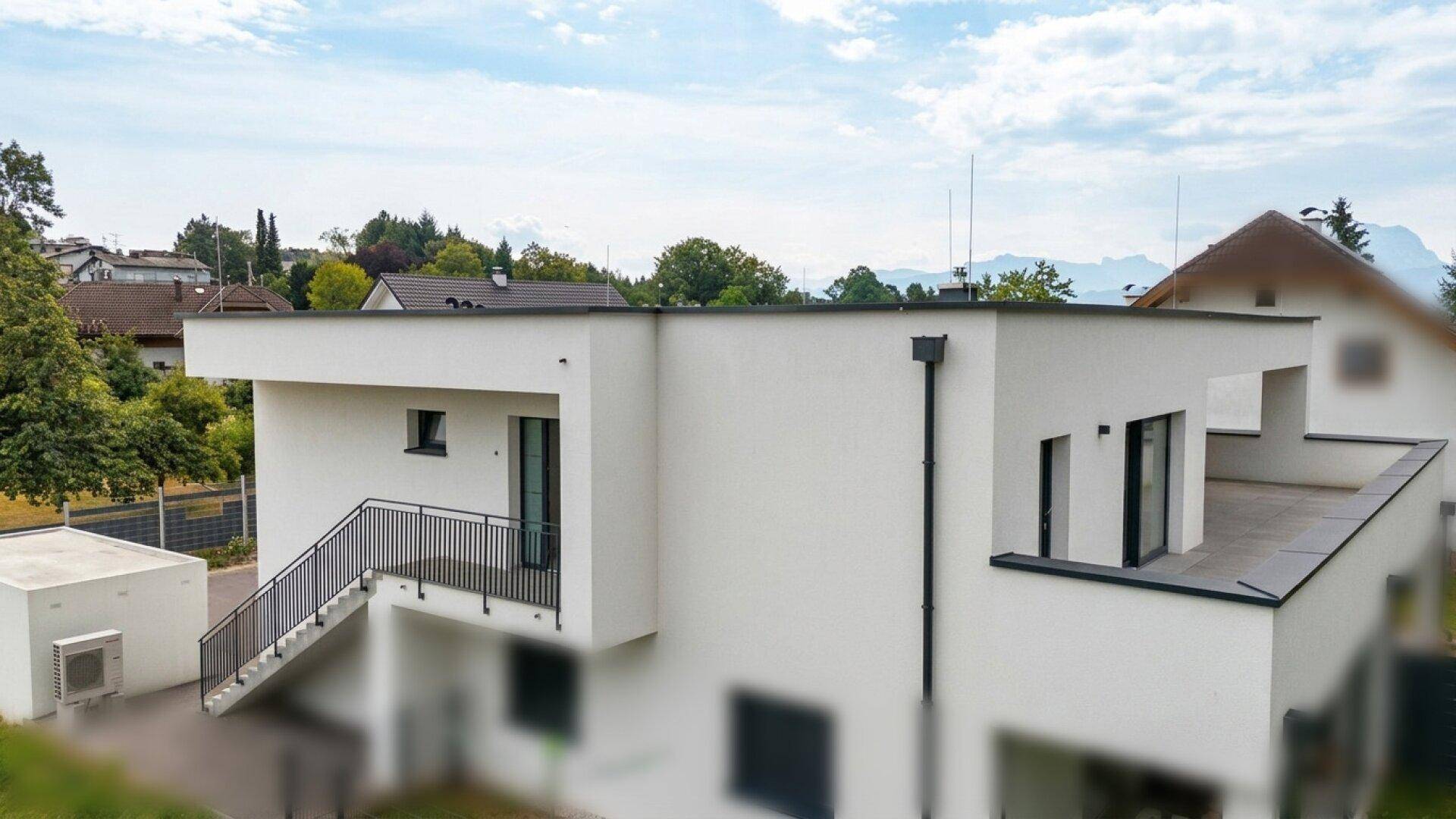 Moderne Architektur des Gebäudes mit weißer Fassade, Flachdach und Außentreppe.
