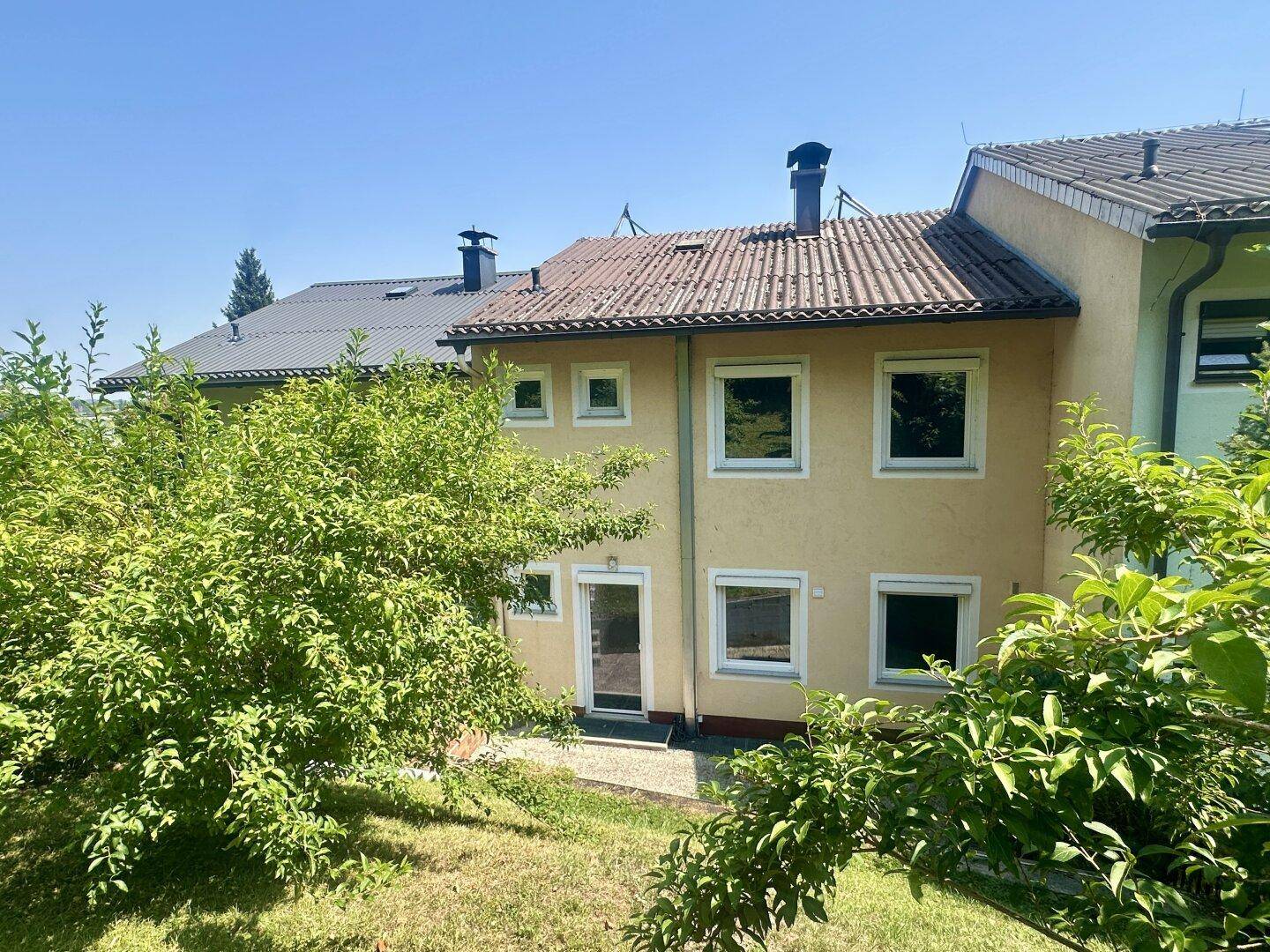 Rückansicht des Reihenhauses mit Garten und grüner Umgebung unter blauem Himmel.