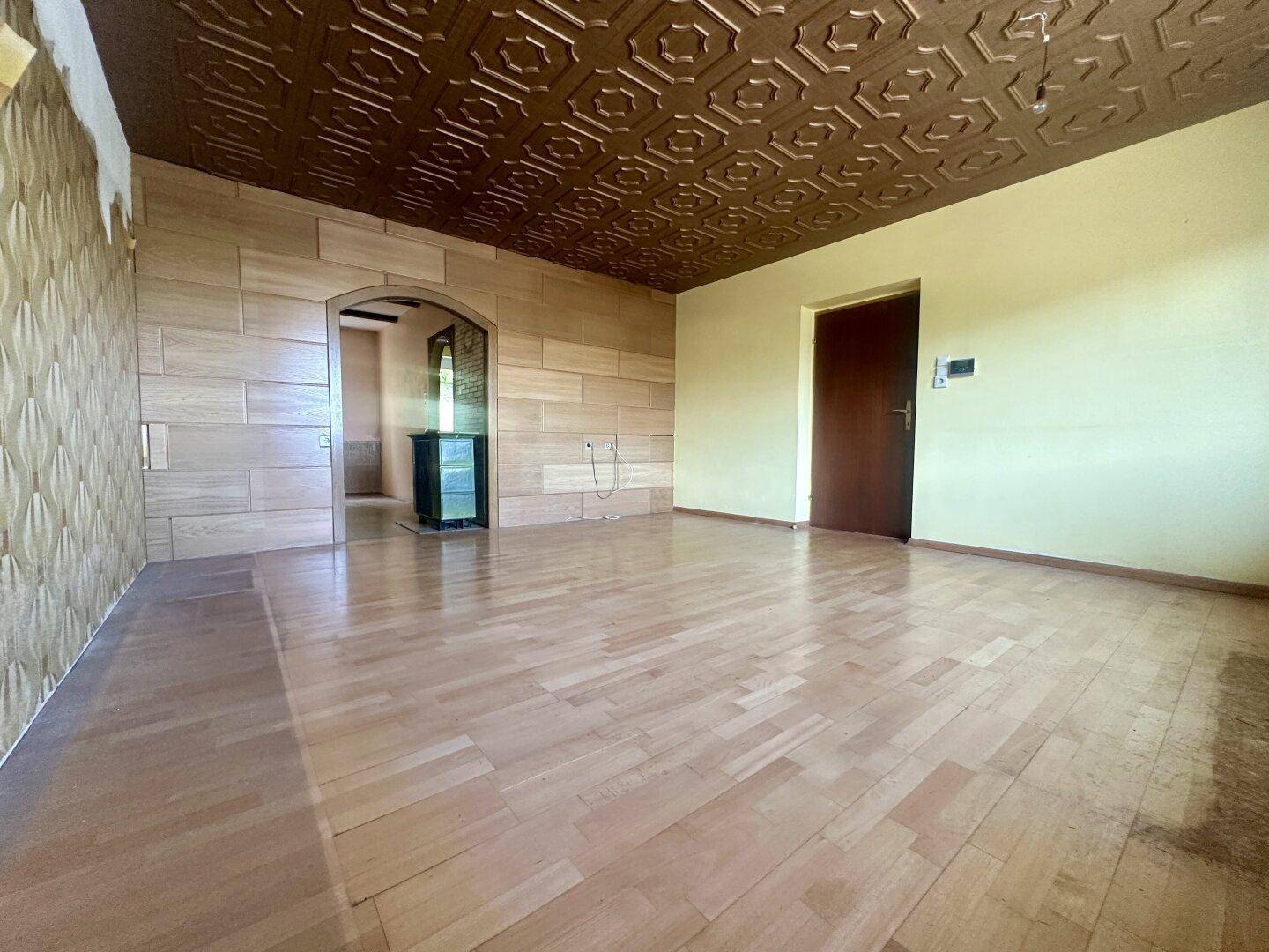 Wohnzimmer mit Parkettboden, Holzwandverkleidung und einem Kaminofen in der Ecke.