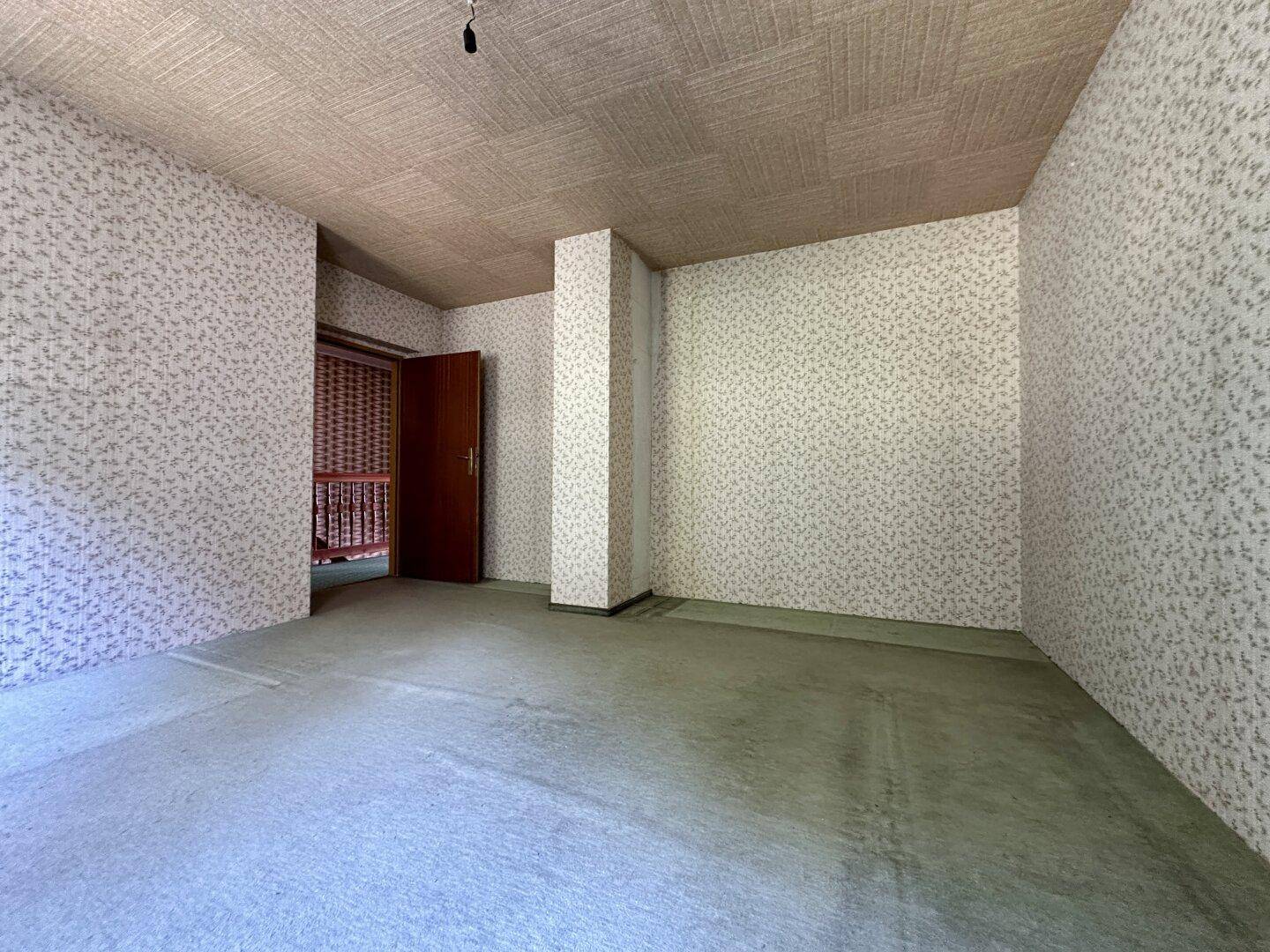 Leeres Zimmer mit gemusterter Tapete und Teppichboden, bereit zur Renovierung.