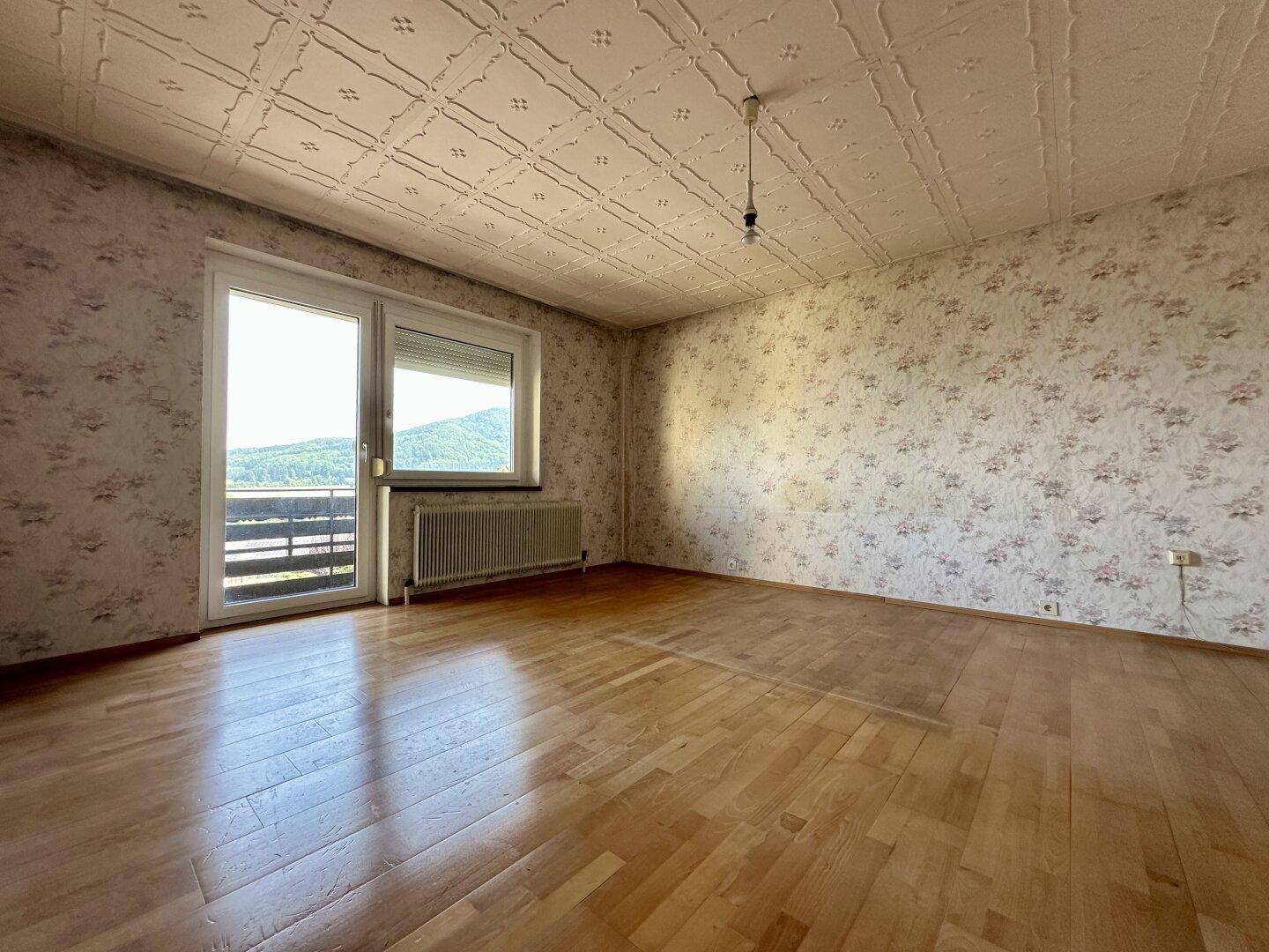 Schlafzimmer mit Parkettboden, Balkonzugang und weitem Blick auf die Landschaft.