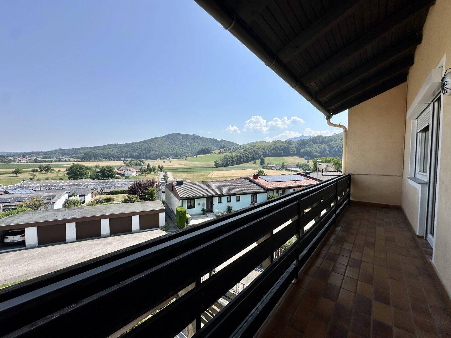 Langer Balkon mit Fliesenboden und Panoramablick auf die grüne Umgebung und Berge.