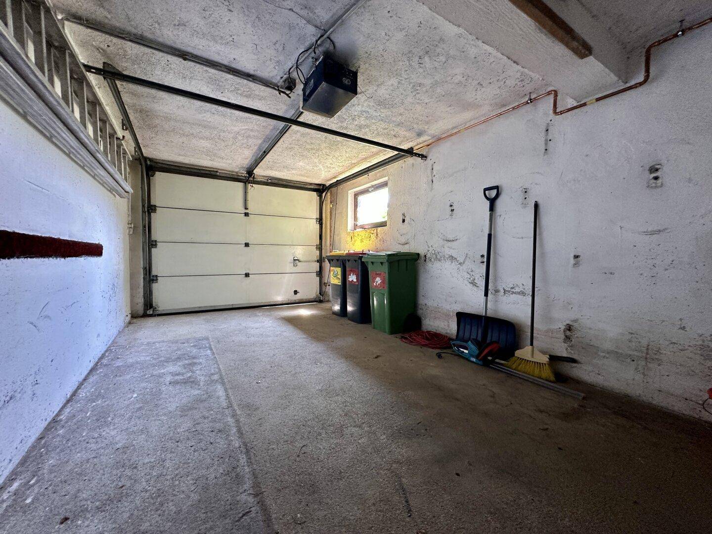 Geräumige Garage mit Rolltor, Fenster und Platz für Mülltonnen.