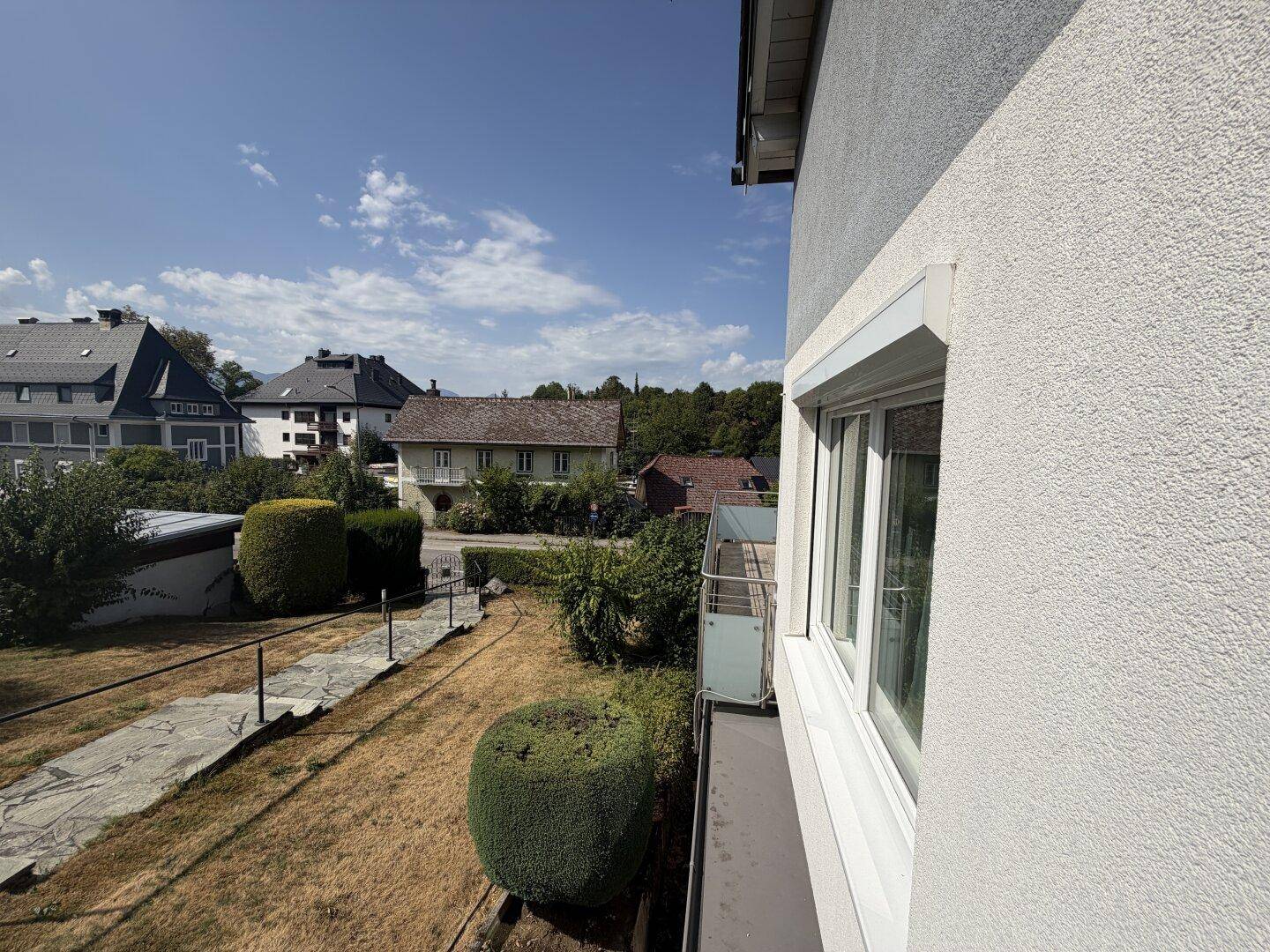 Ausblick von einem Balkon auf die grüne Umgebung und weitere Häuser.