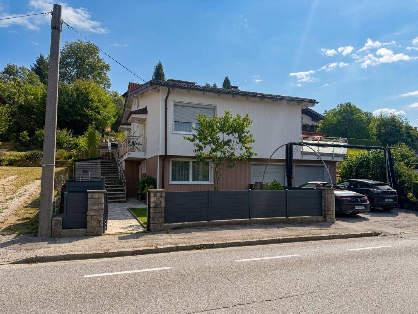 Ansicht des Hauses von der Straße mit Garage, Zaun und Zugang über eine Treppe.