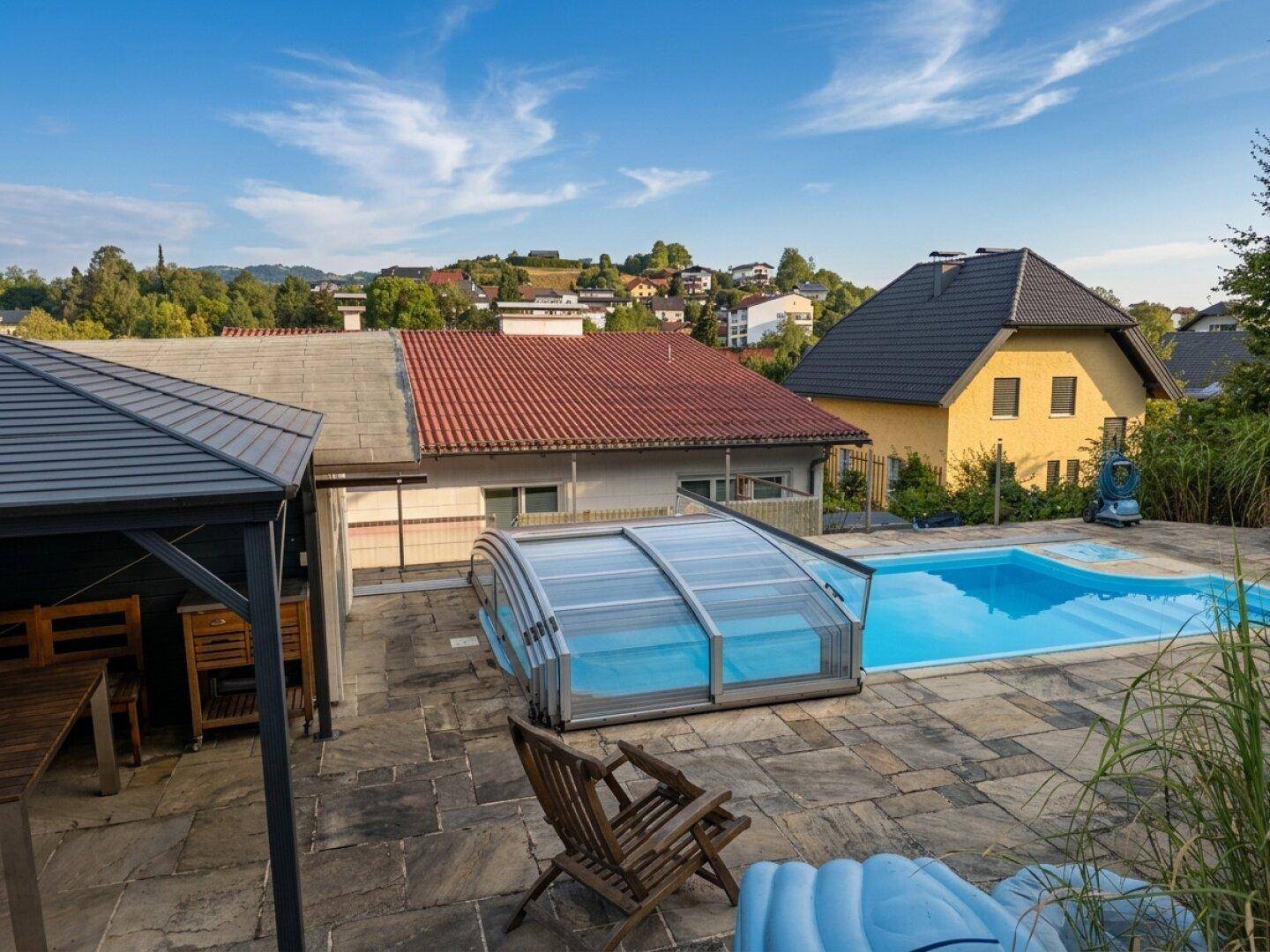 Panoramablick auf den Poolbereich und die umliegende Hügellandschaft unter blauem Himmel.