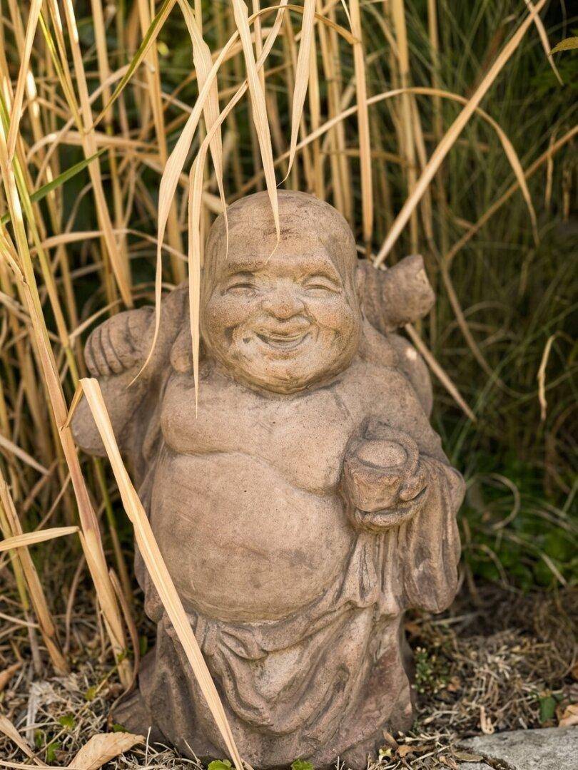 Nahaufnahme einer Buddha-Statue im hohen Gras, die eine ruhige Gartendekoration darstellt.