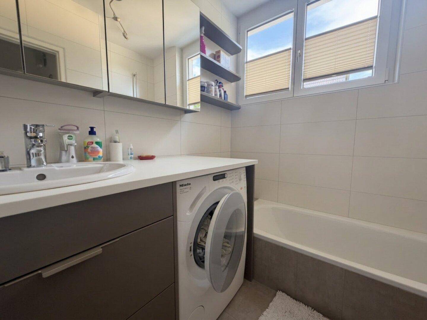 Badezimmer mit Waschbecken, Spiegelschrank, Badewanne und integrierter Waschmaschine.