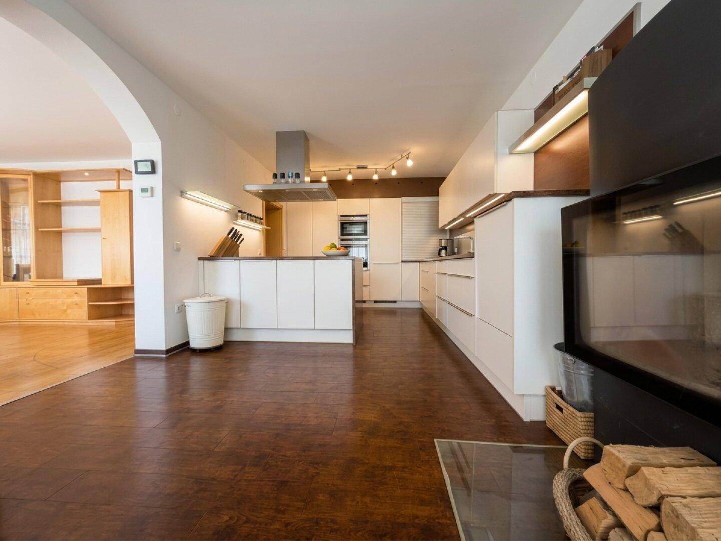 Offene Küche und Wohnbereich mit Kamin, weißen Schränken und dunklem Boden.