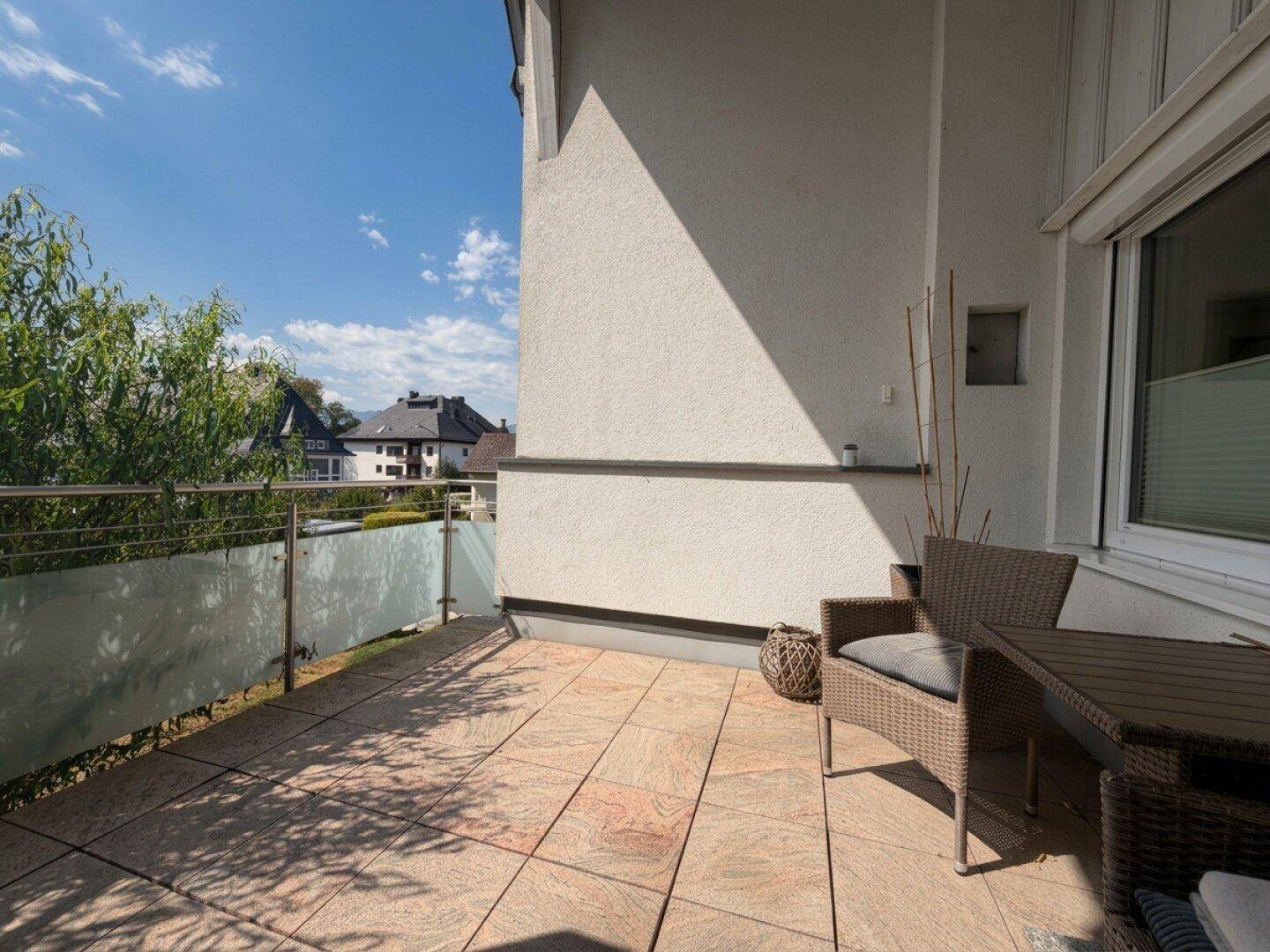 Geräumiger Balkon mit Fliesenboden, Rattanmöbeln und Blick auf die Nachbarschaft.