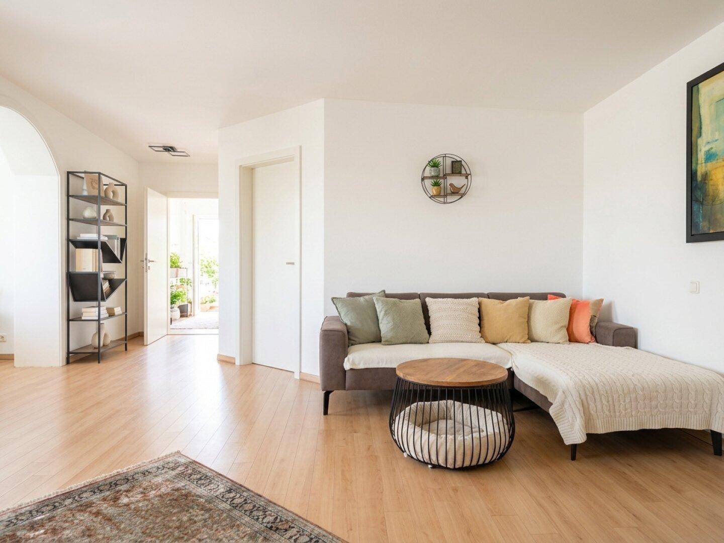 Wohnzimmer mit grauem Ecksofa, rundem Couchtisch und hellem Holzboden, offen und einladend.