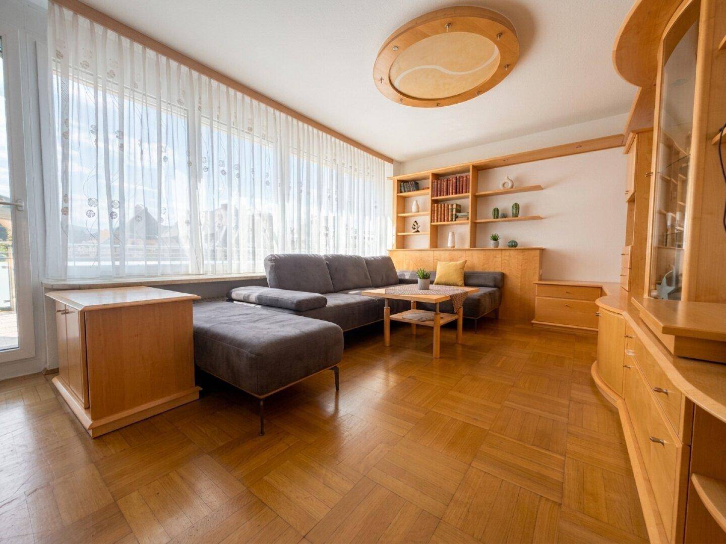 Geräumiges Wohnzimmer mit großem Ecksofa, maßgefertigten Holzregalen und viel Tageslicht.