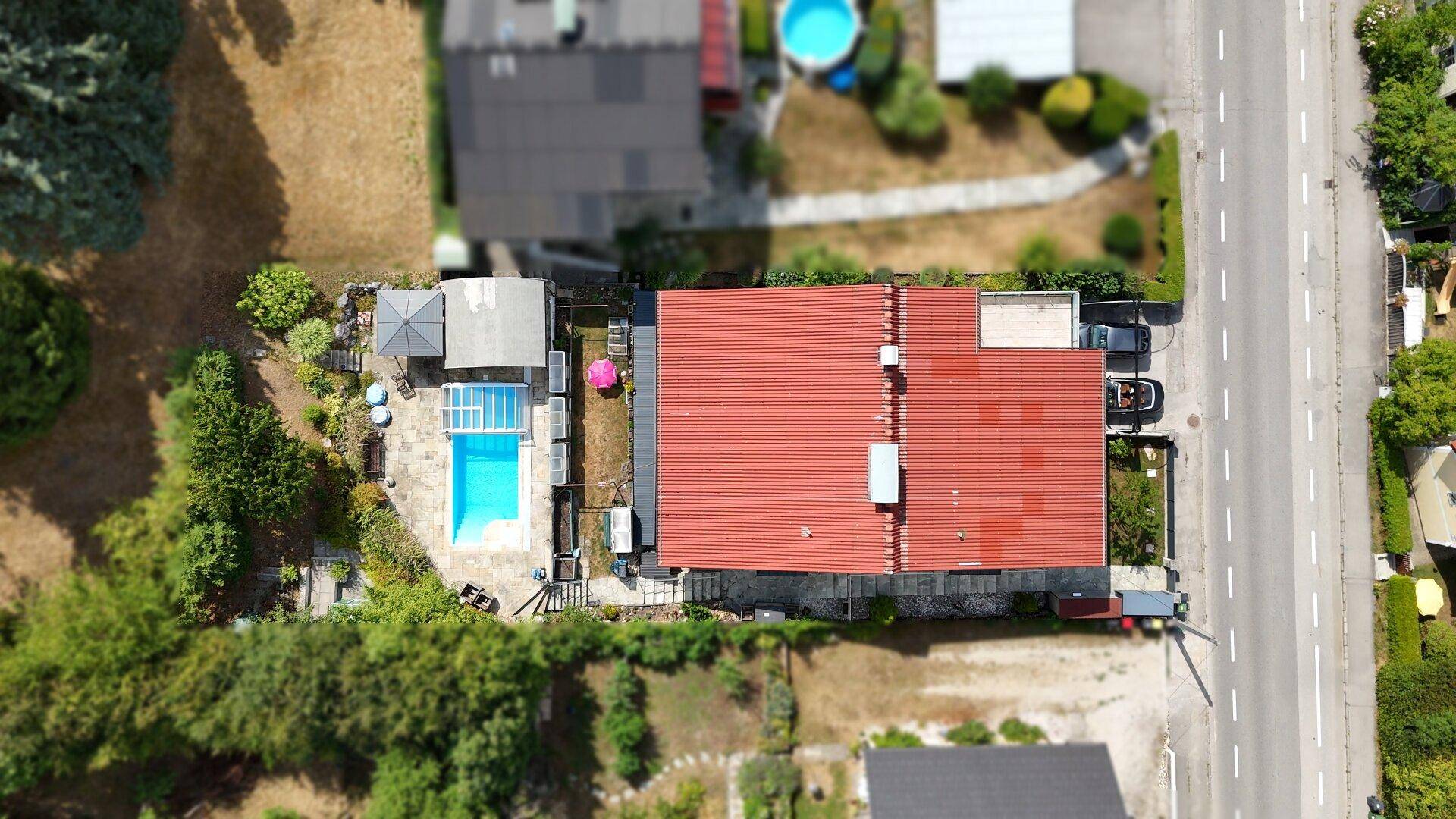 Gesamtansicht des Anwesens von oben mit Haus, Poolbereich, Garten und angrenzender Straße.