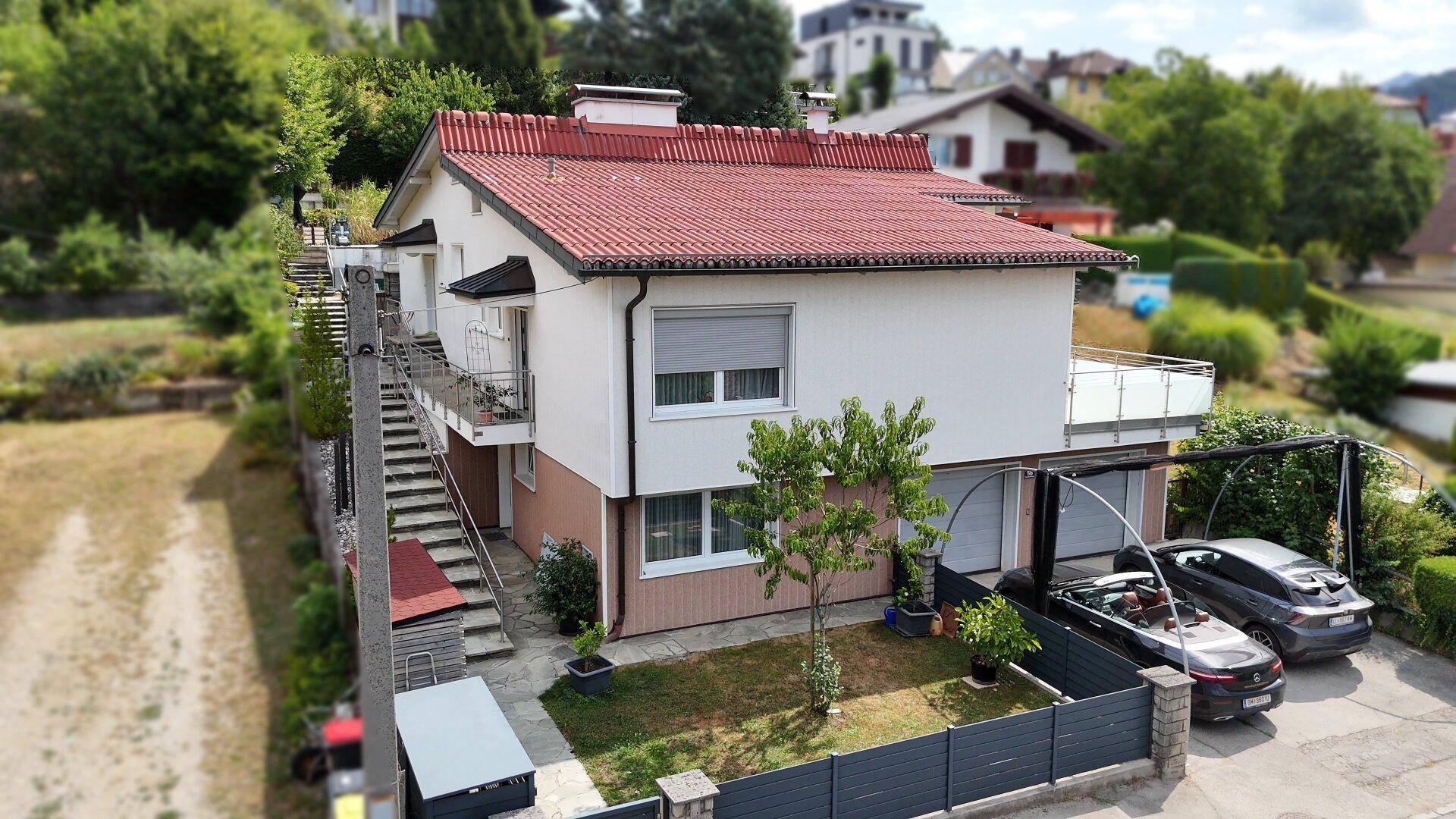 Seitenansicht des Hauses mit Außentreppe, kleinem Vorgarten und überdachtem Parkplatz.