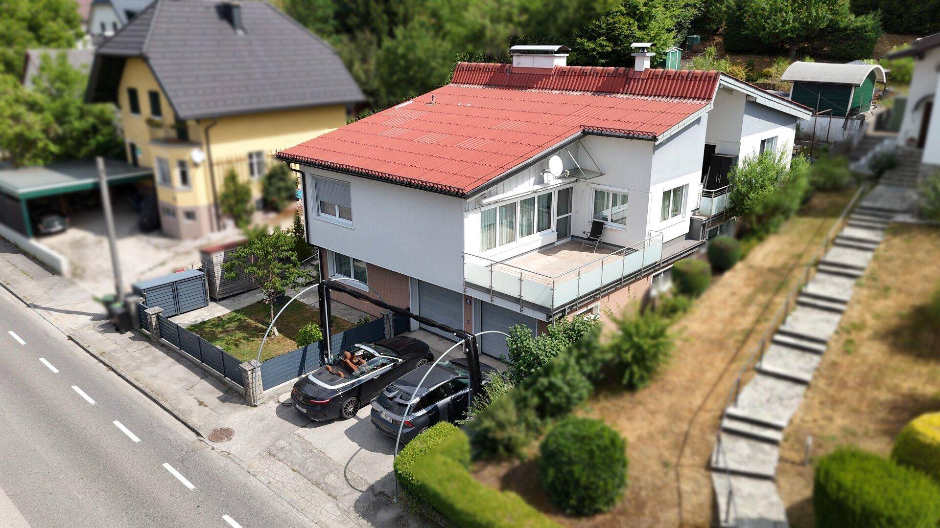 Vogelperspektive des Hauses mit rotem Dach, zwei Garagen und gepflasterter Auffahrt.