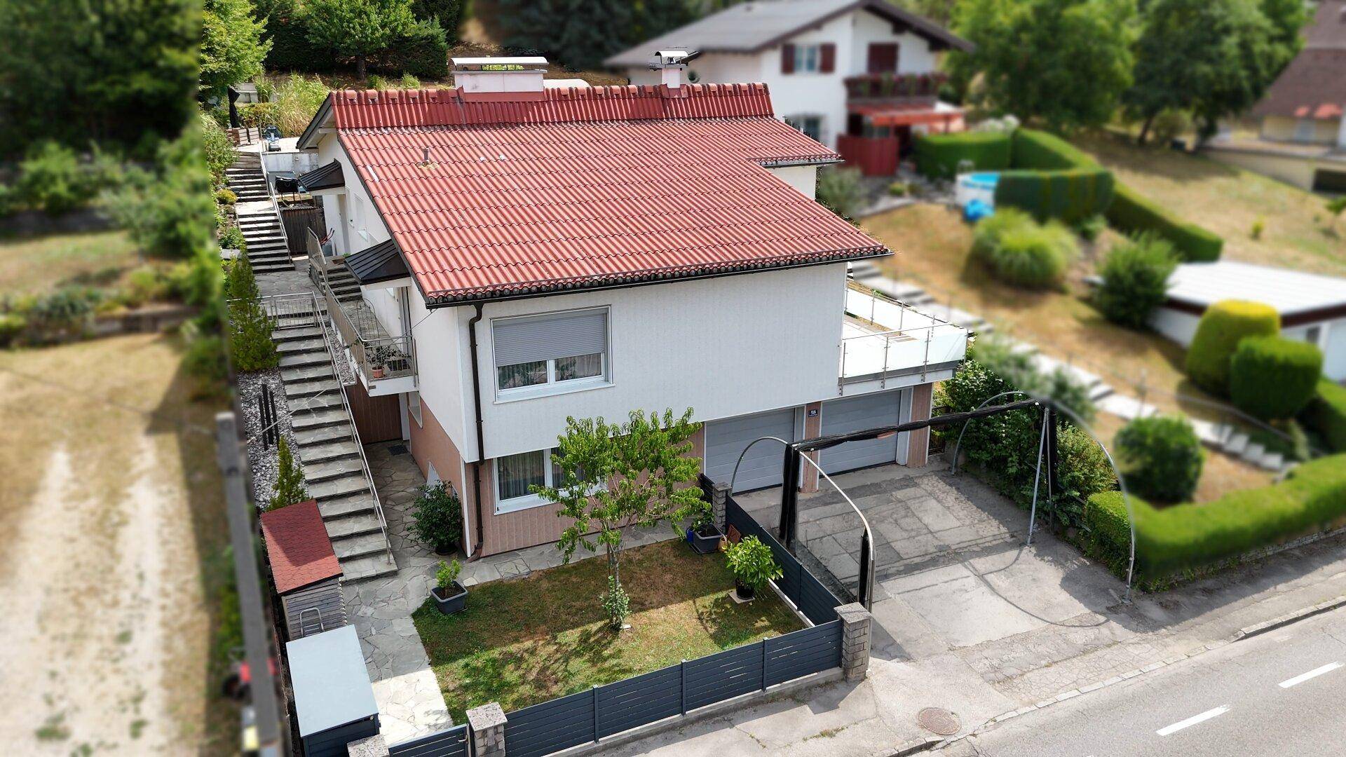 Luftaufnahme eines Wohnhauses mit rotem Ziegeldach, Garage und gepflegtem Vorgarten.