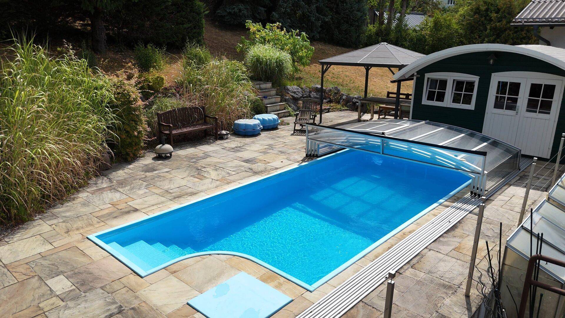 Großzügiger Poolbereich mit gepflasterter Terrasse, Holzbank und Gartenhaus, ideal zum Entspannen.