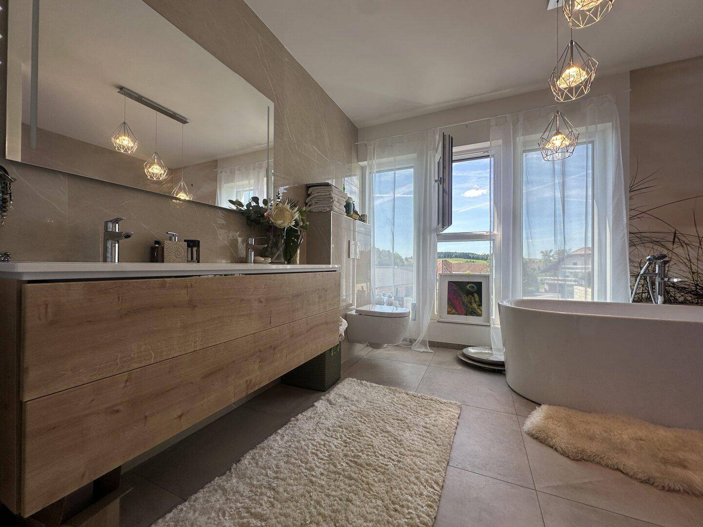 Modernes Badezimmer mit freistehender Badewanne, Holzwaschtisch und großen Fenstern mit Ausblick.