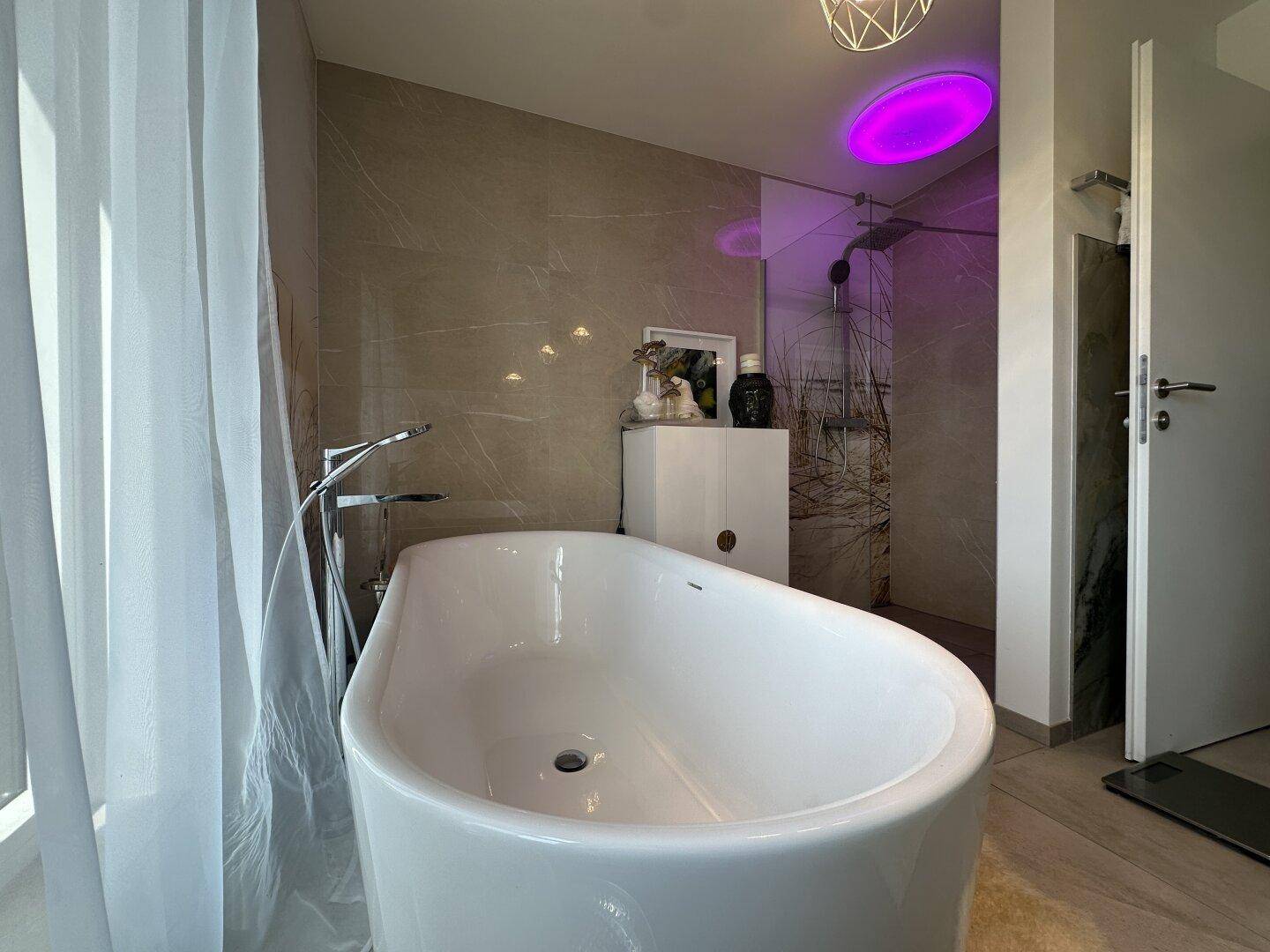 Elegantes Badezimmer mit freistehender Badewanne, Glasdusche und stimmungsvoller Beleuchtung.