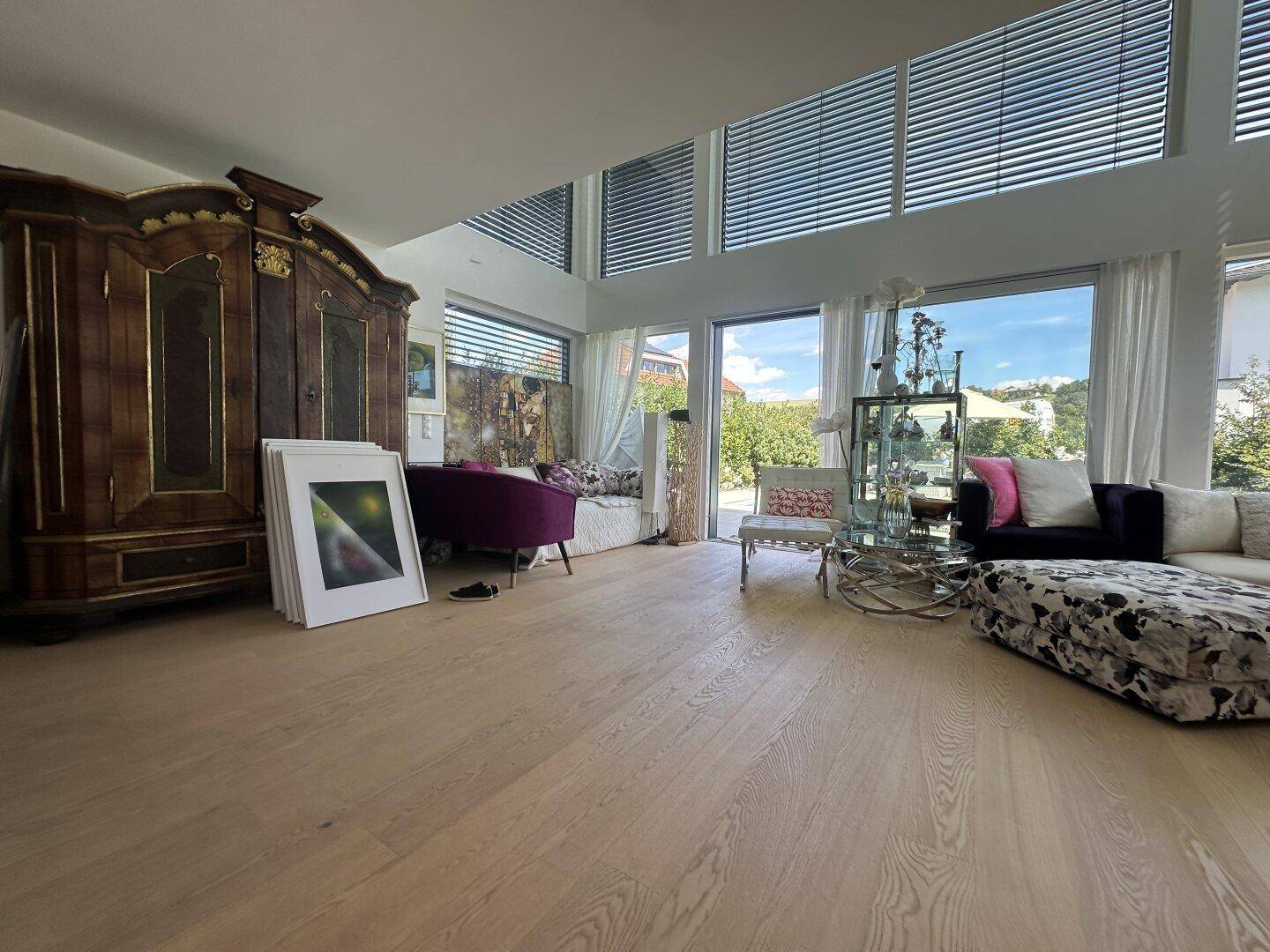 Helles Wohnzimmer mit Holzboden, großen Fenstern und einer Mischung aus modernen und antiken Möbeln.