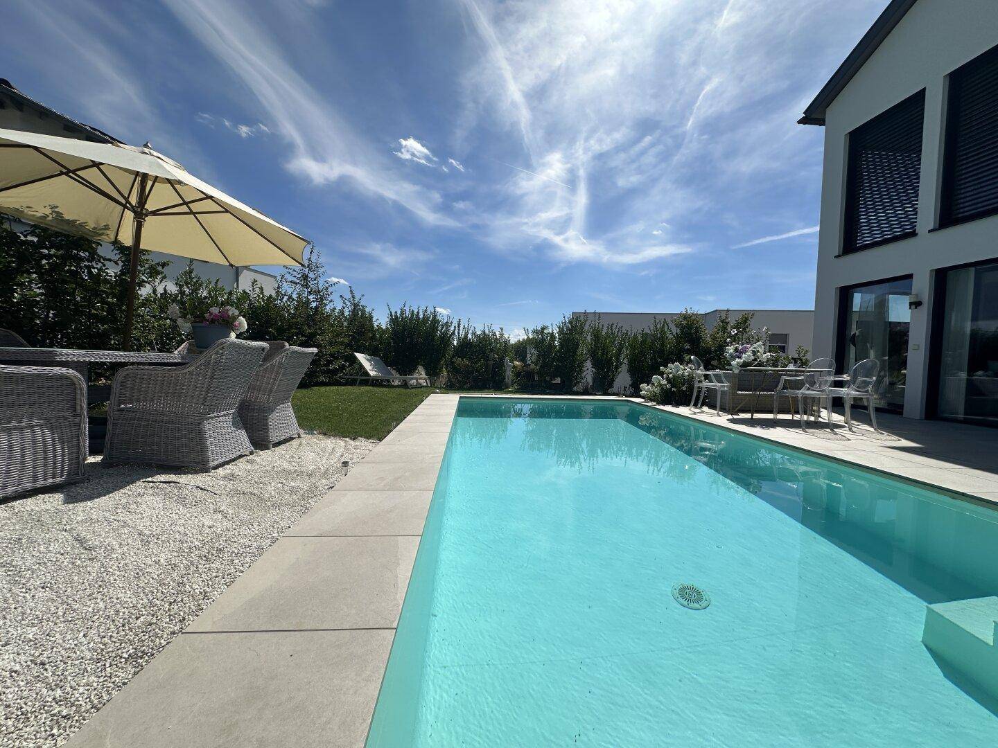 Weitläufiger Poolbereich mit Liegestühlen, Sonnenschirm und Blick auf das moderne Haus.